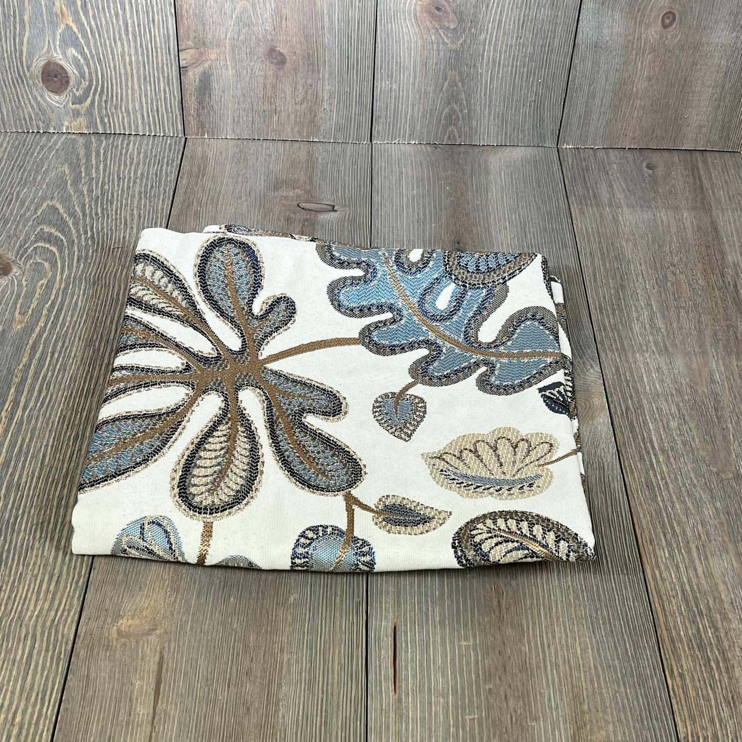 Jacquard tropical leaf pattern throw pillow cover in blue and cream, folded on a wooden surface, 20x20 inches.