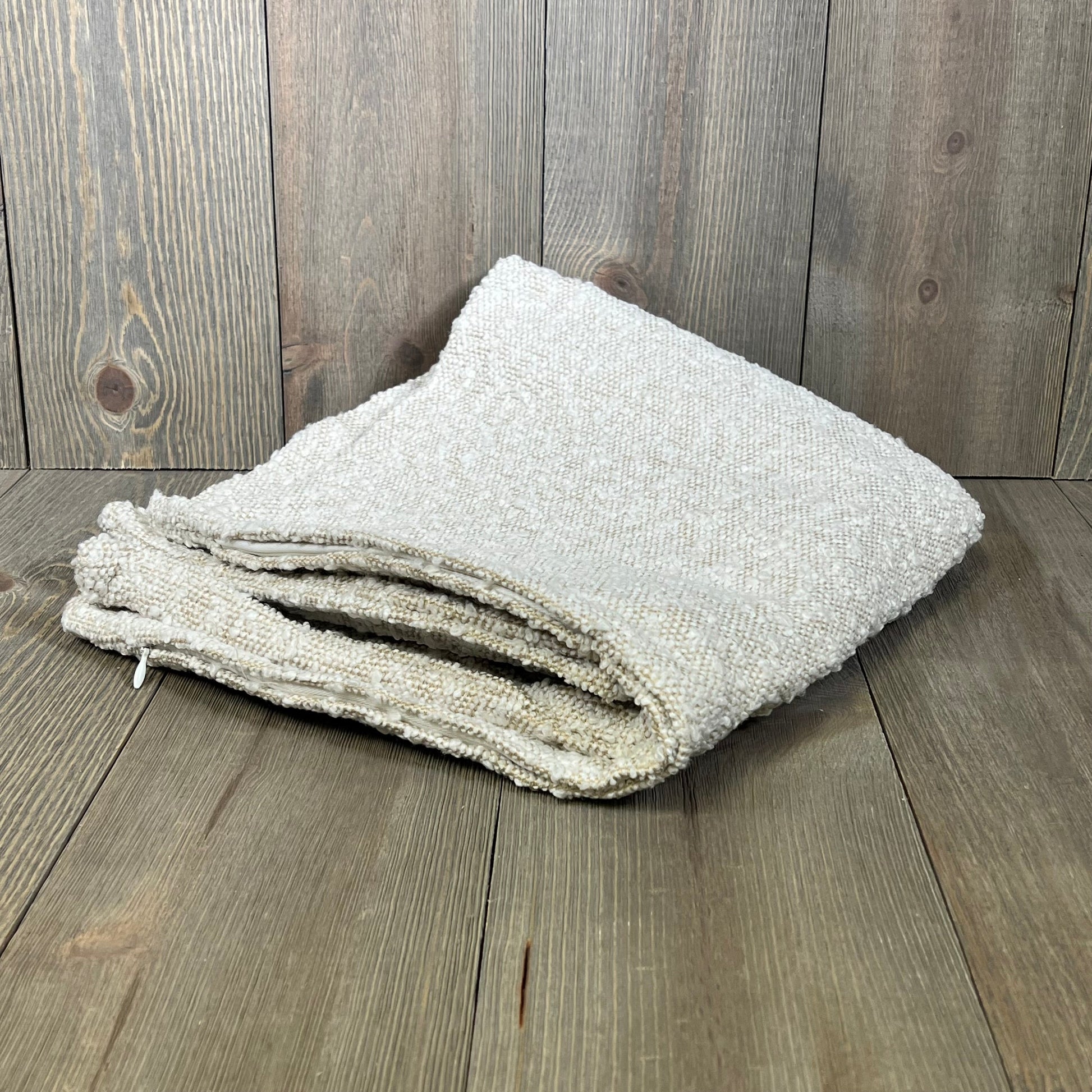 Ivory boucle throw pillow cover folded on wooden floor, 24x24 inch, perfect for modern living room decor.