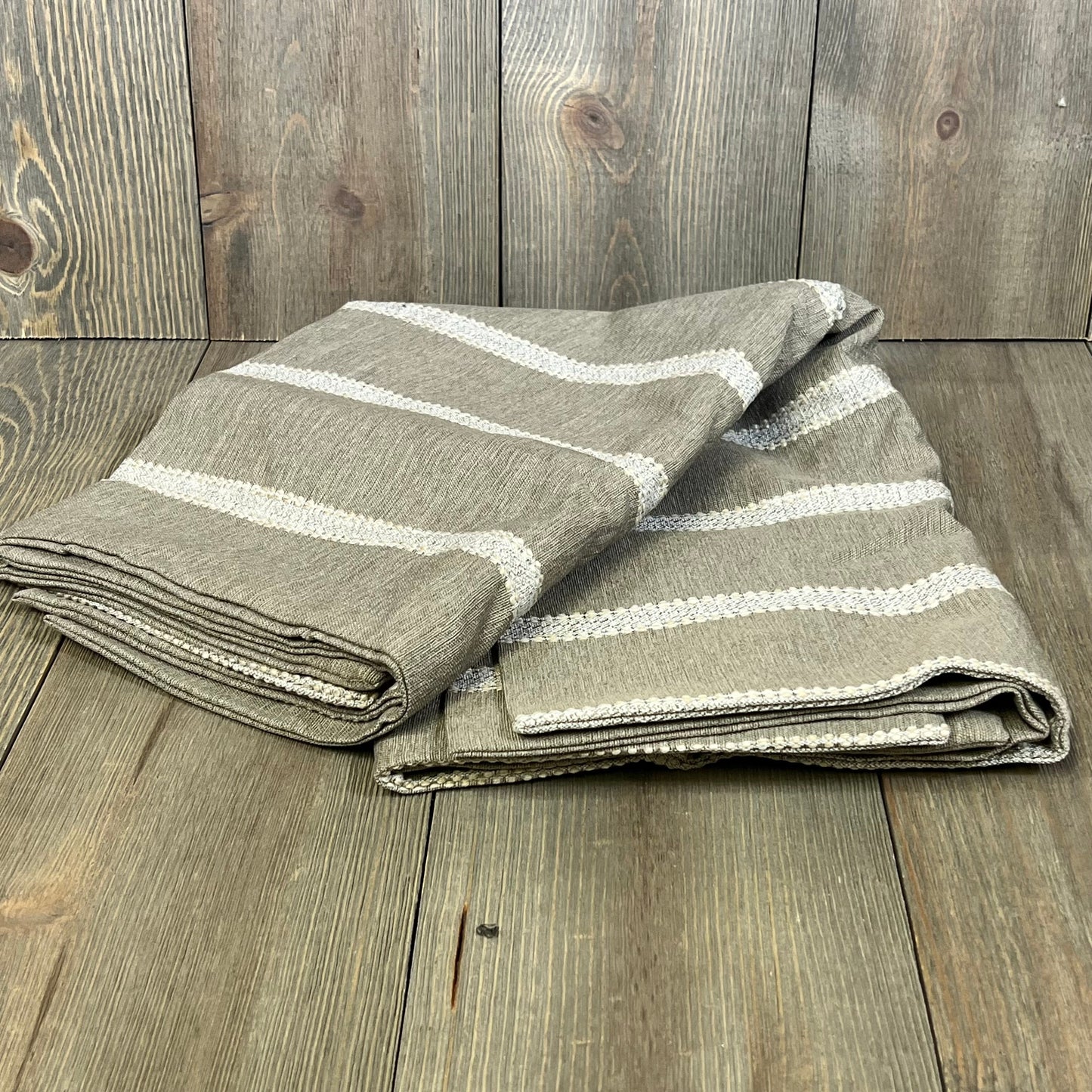 Tan striped decorative pillow covers, 24x24 inches, folded neatly on a rustic wooden surface, perfect for living room decor.
