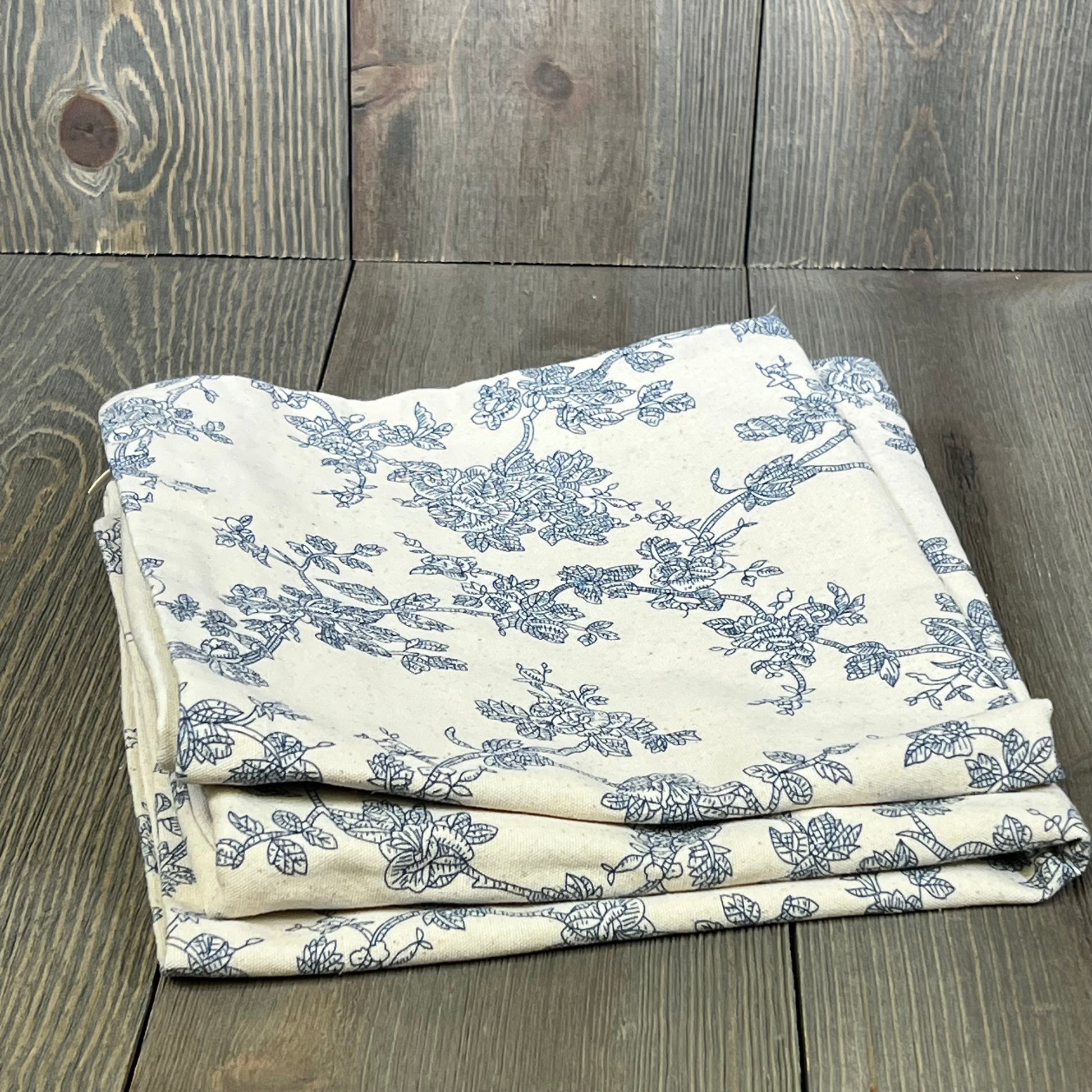 Blue and white floral 100% cotton throw pillow covers set, folded on rustic wood, 16x16-inch, perfect for farmhouse decor.