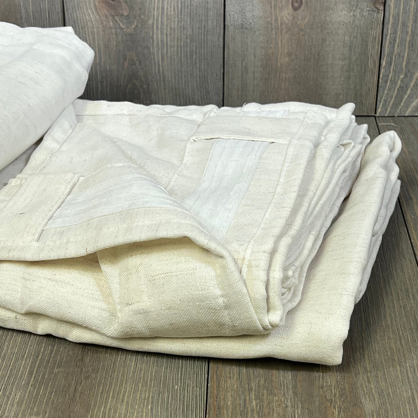 Cream linen curtains folded neatly, showcasing pleated back tab design, ideal for wide windows and sliding doors.