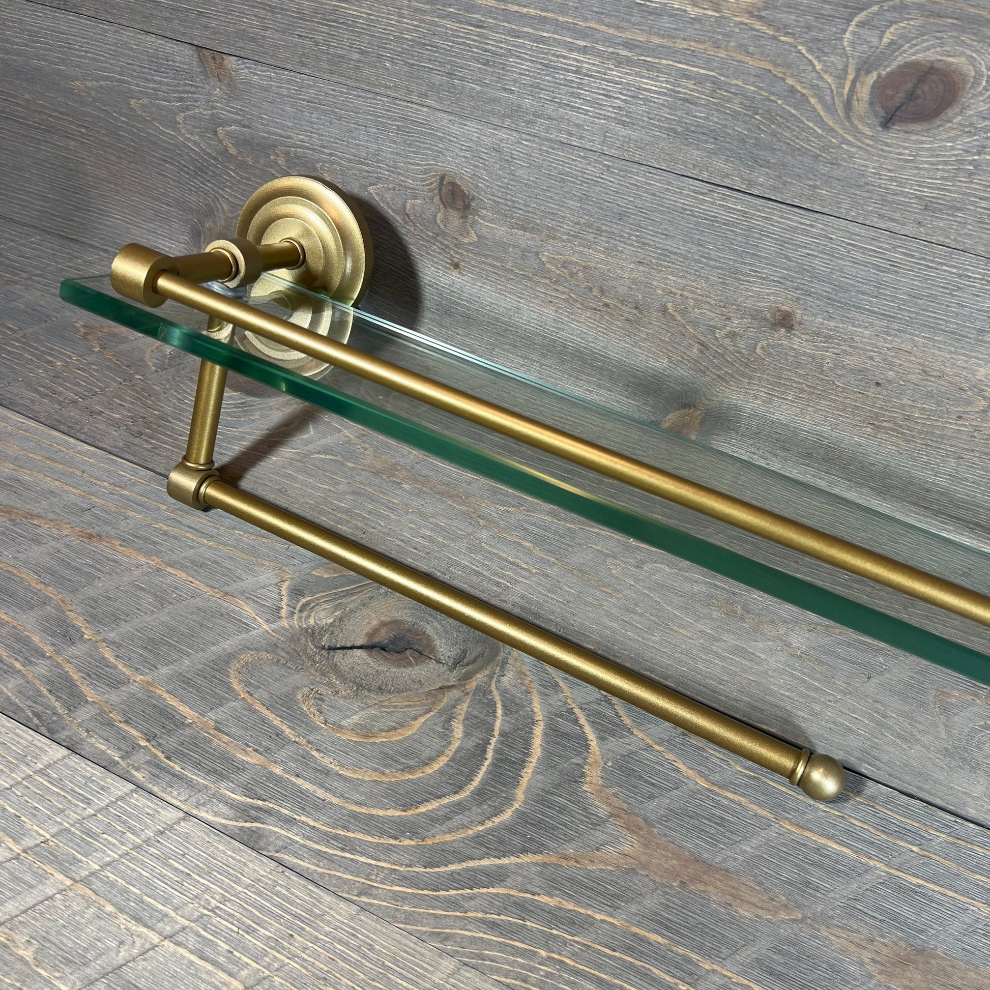 Gold-finished paper towel holder with 22-inch glass shelf, mounted on wooden background.