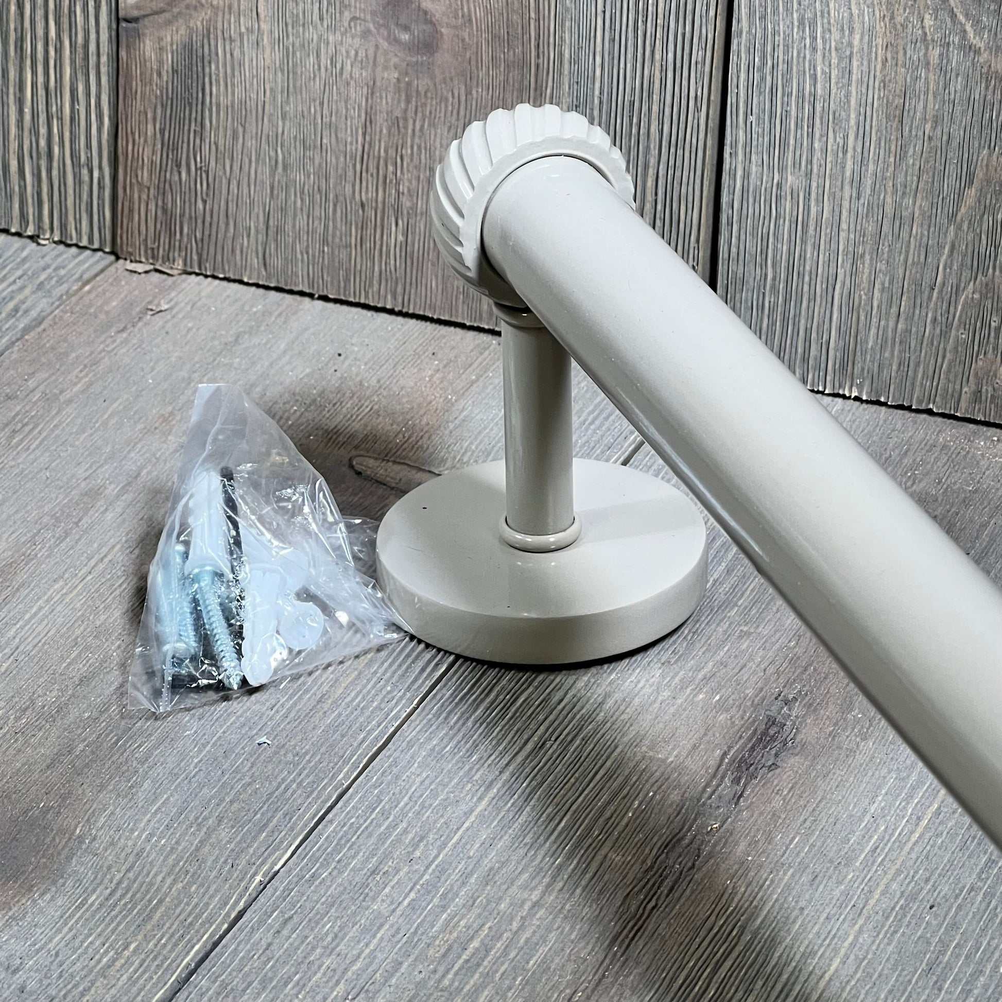 Shaded beige towel bar with twist detail and mounting hardware on a wooden floor.