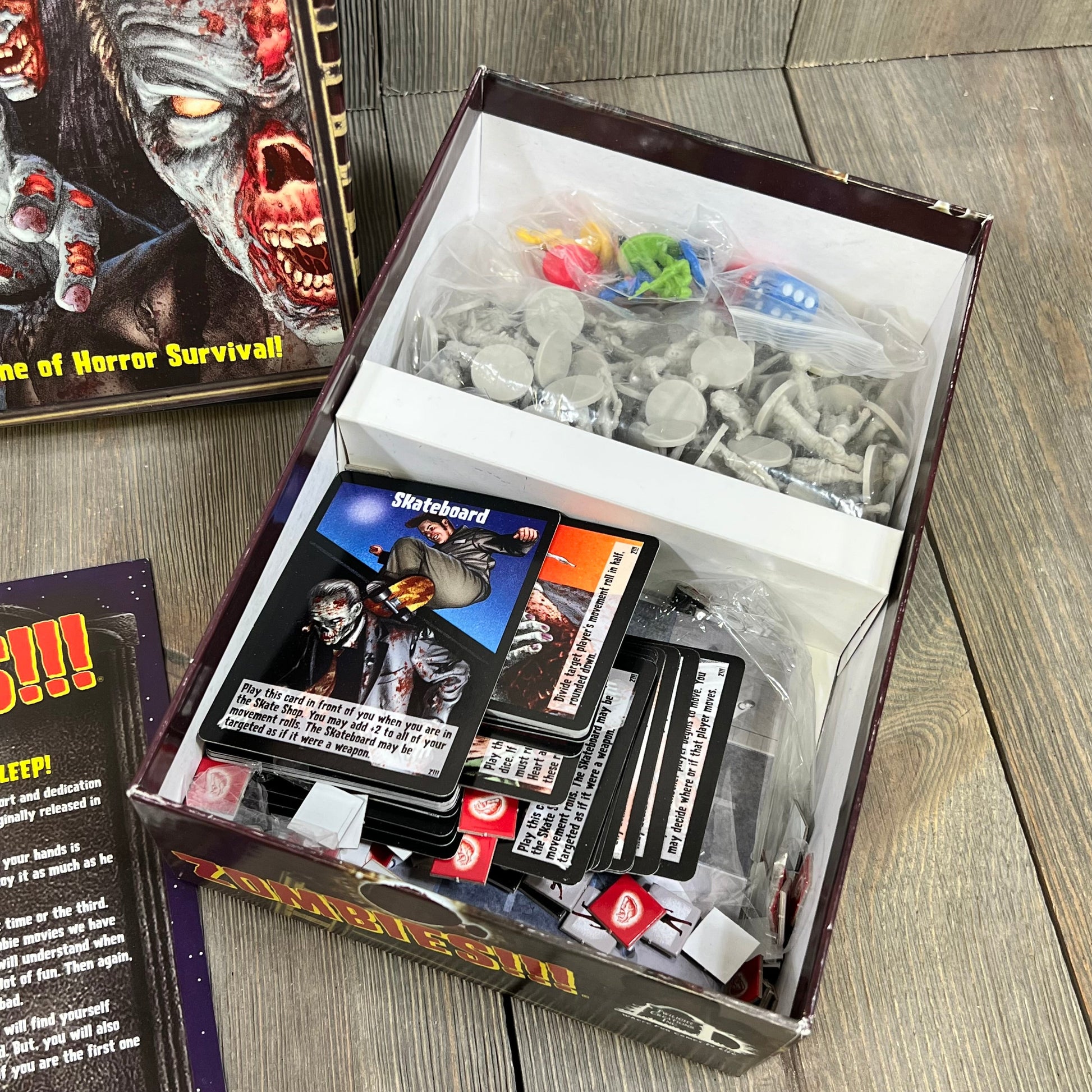 Open box of the Twilight Creations Zombies Third Edition board game, featuring cards, miniatures, and colorful player pieces.