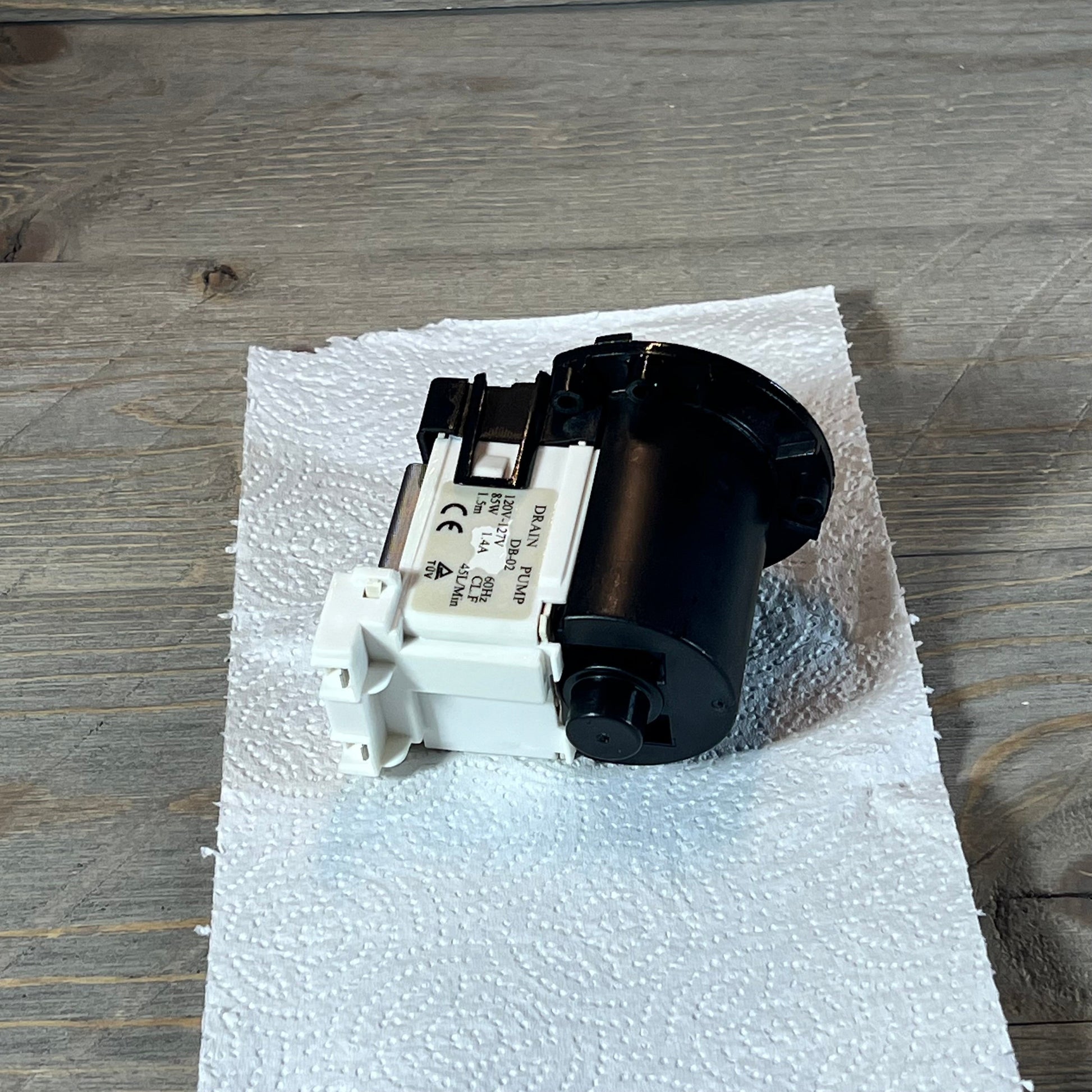 Kenmore & LG washer drain pump motor on paper towel, showcasing compact design.