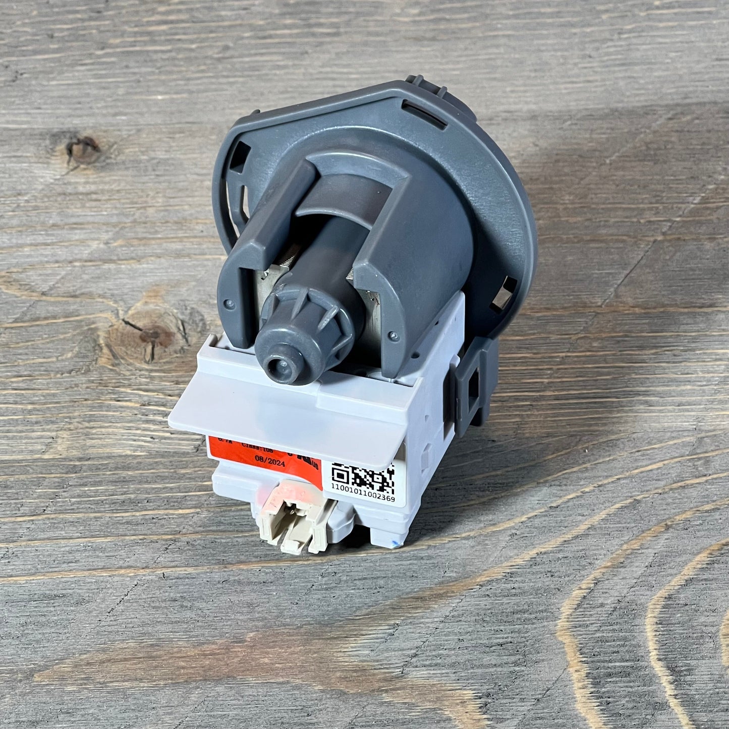 Kenmore Frigidaire dishwasher drain pump assembly on wooden surface, showcasing compact design and connection ports.