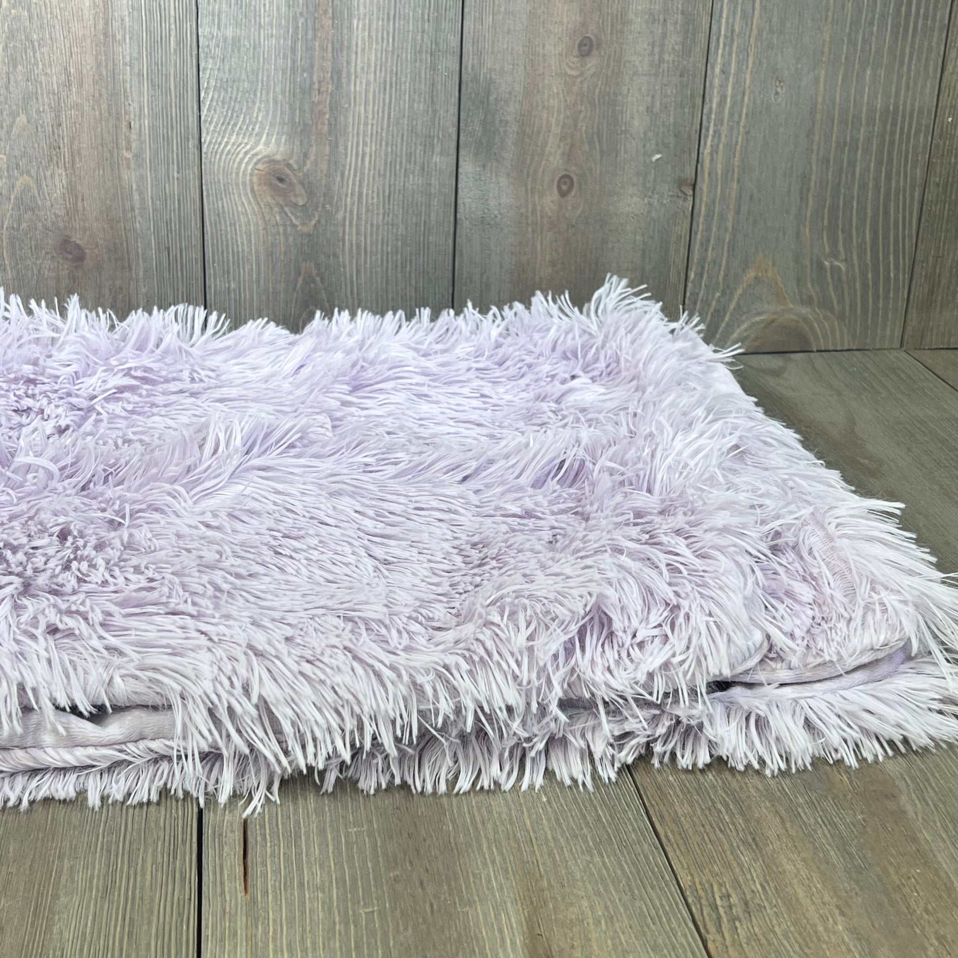 Fluffy light purple faux fur pillowcases with zipper closure on a wooden background. Cozy and decorative for any room.