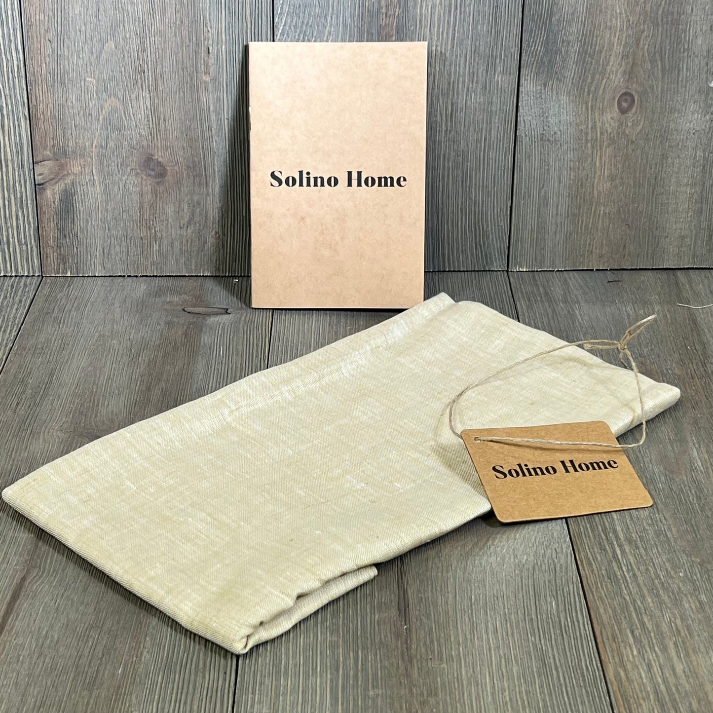 Champagne beige linen table runner by Solino Home, folded, with tag on wooden surface, ideal for dressers and coffee tables.