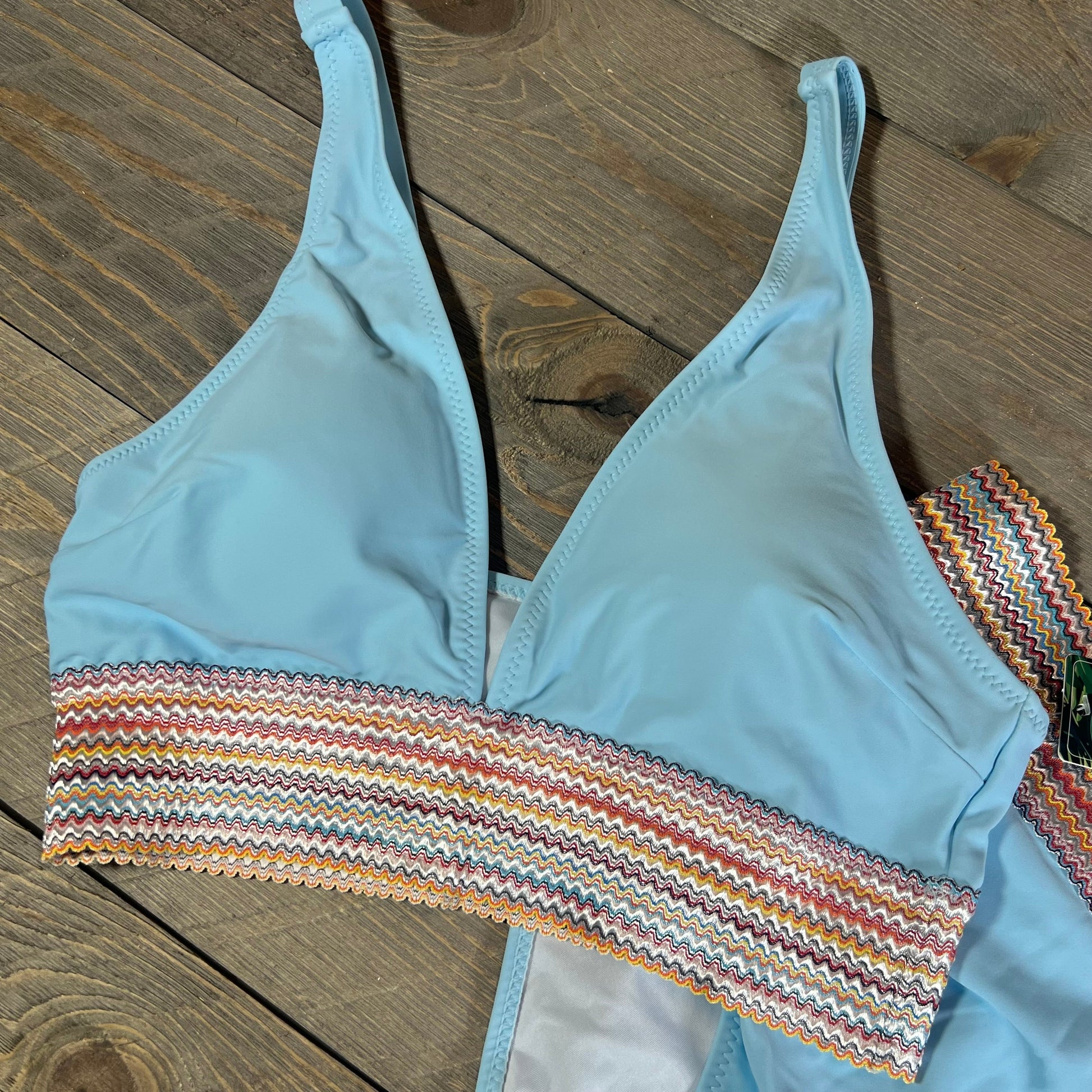 Light blue bikini top with colorful zigzag waistband on wooden background, part of the Blooming Jelly high waisted set.