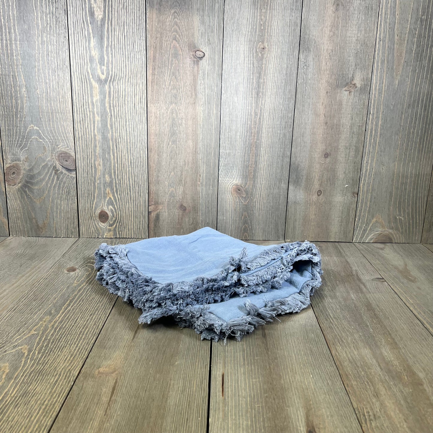Light blue throw pillow covers with fringe and tassels, perfect for boho farmhouse decor, folded on a wooden surface.