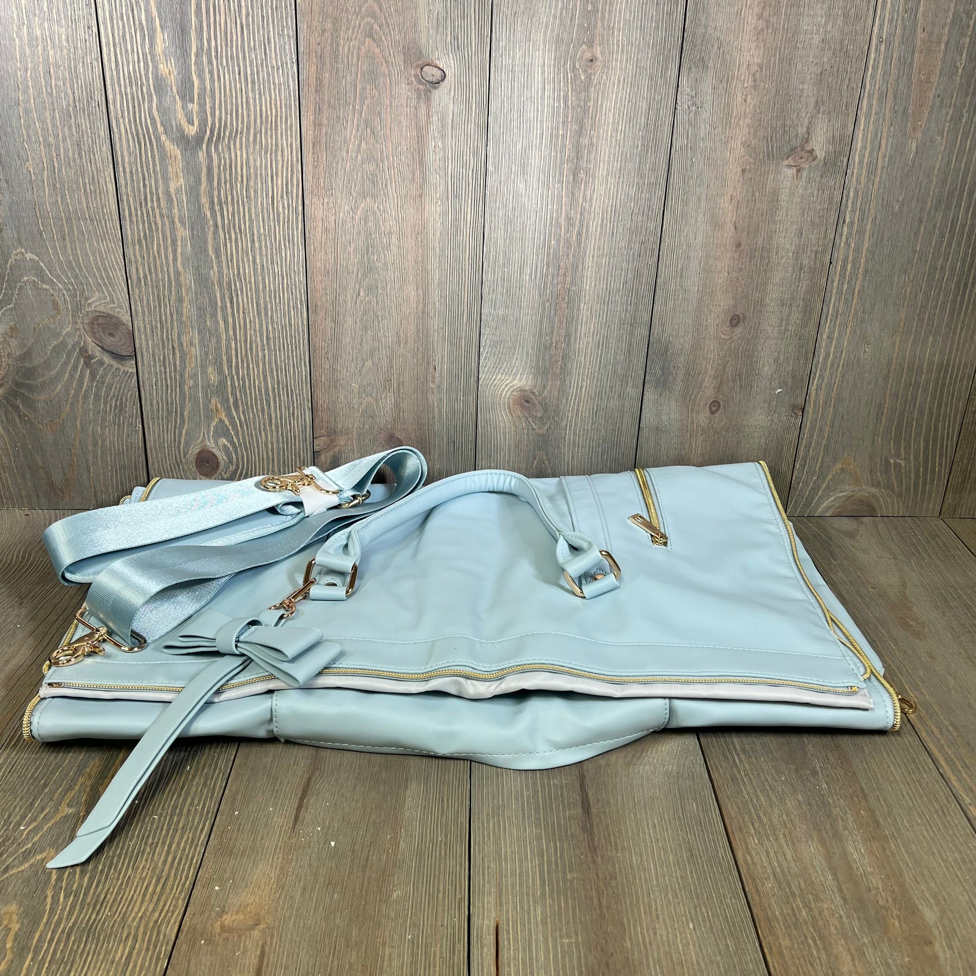 Blue convertible garment bag for travel, featuring a shoulder strap and zippered compartments, stylish and functional design.