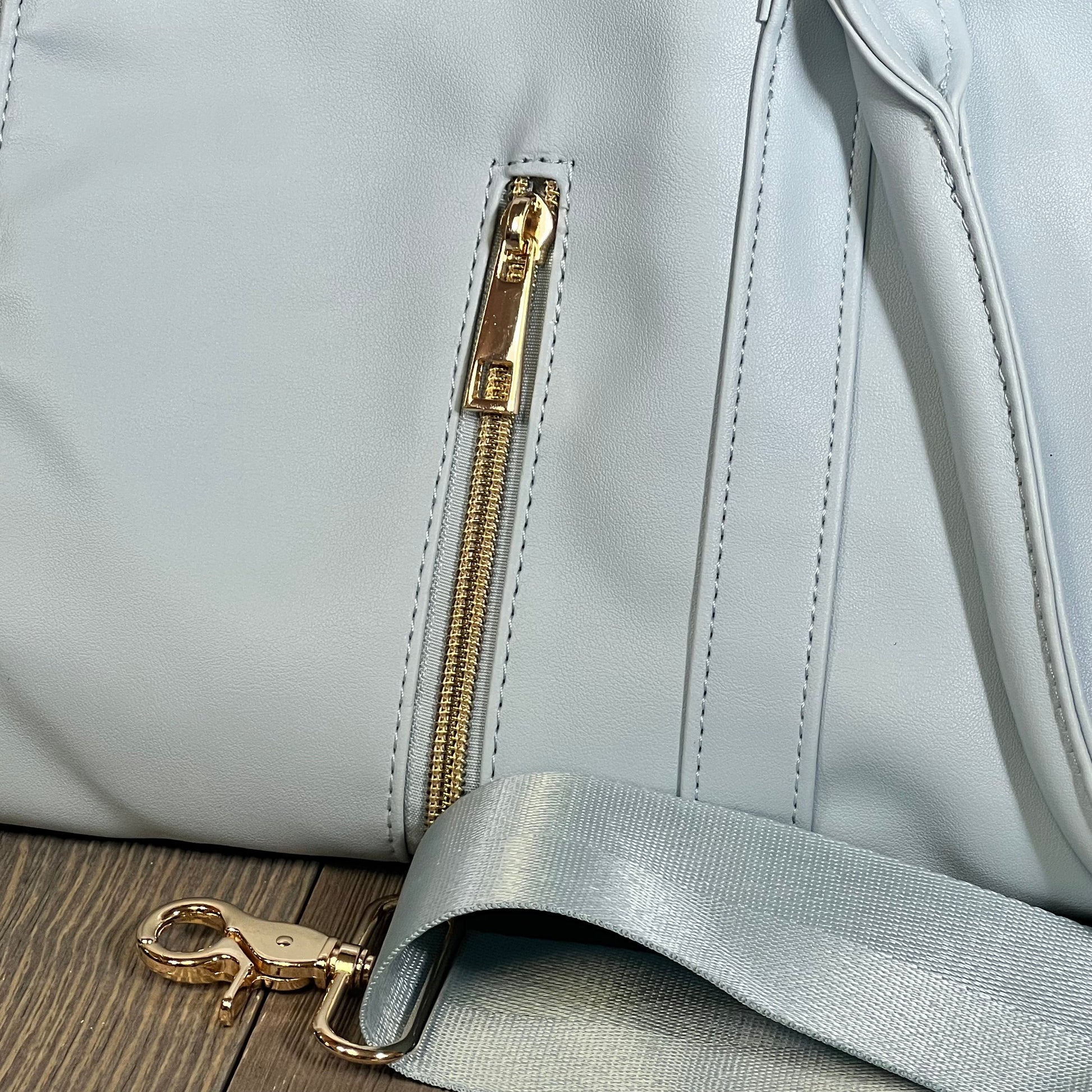 Blue PU leather travel garment bag with gold zipper and detachable shoulder strap, perfect for stylish women on the go.