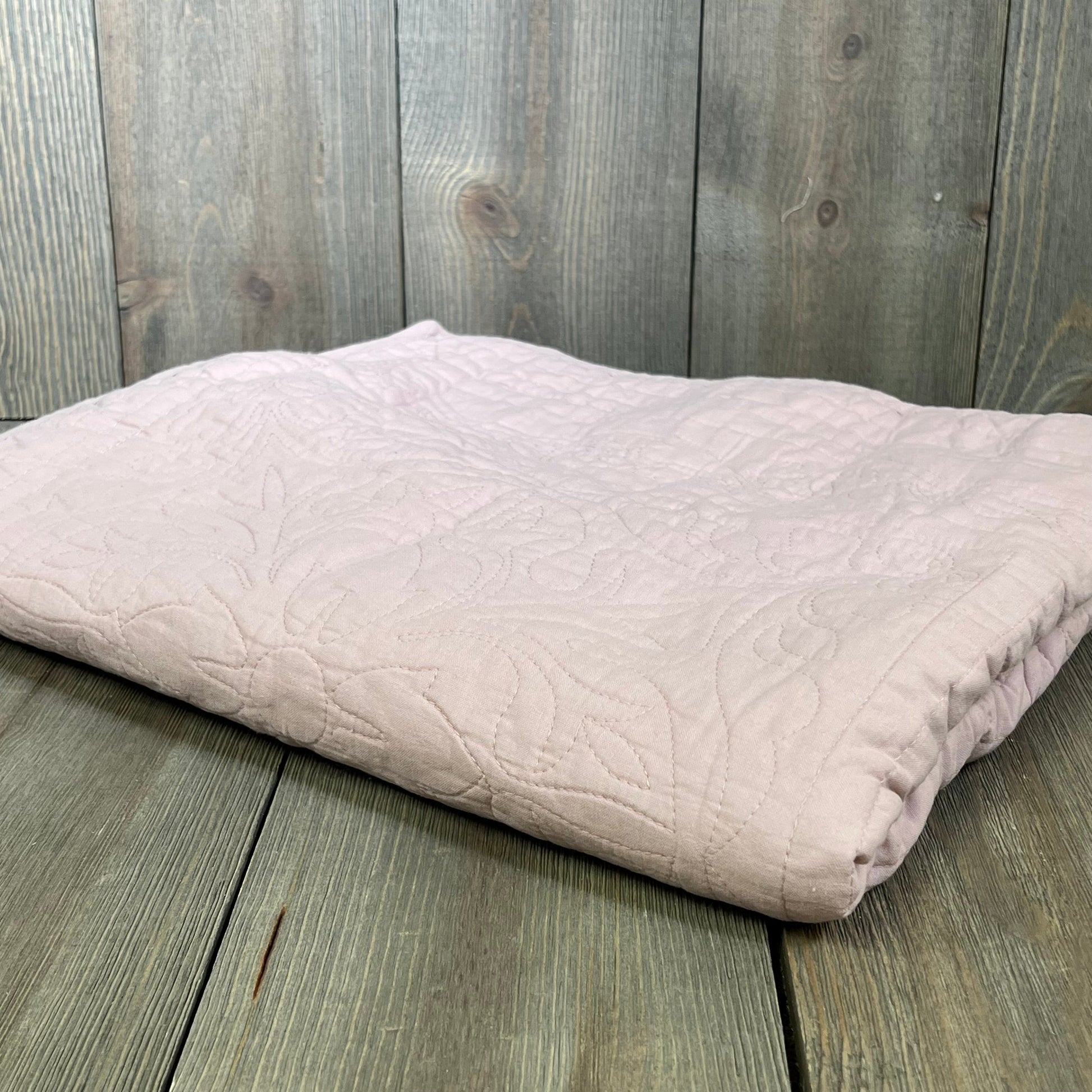 Dusty pink cotton quilted pillow sham with floral print, folded on a wooden surface, standard size.
