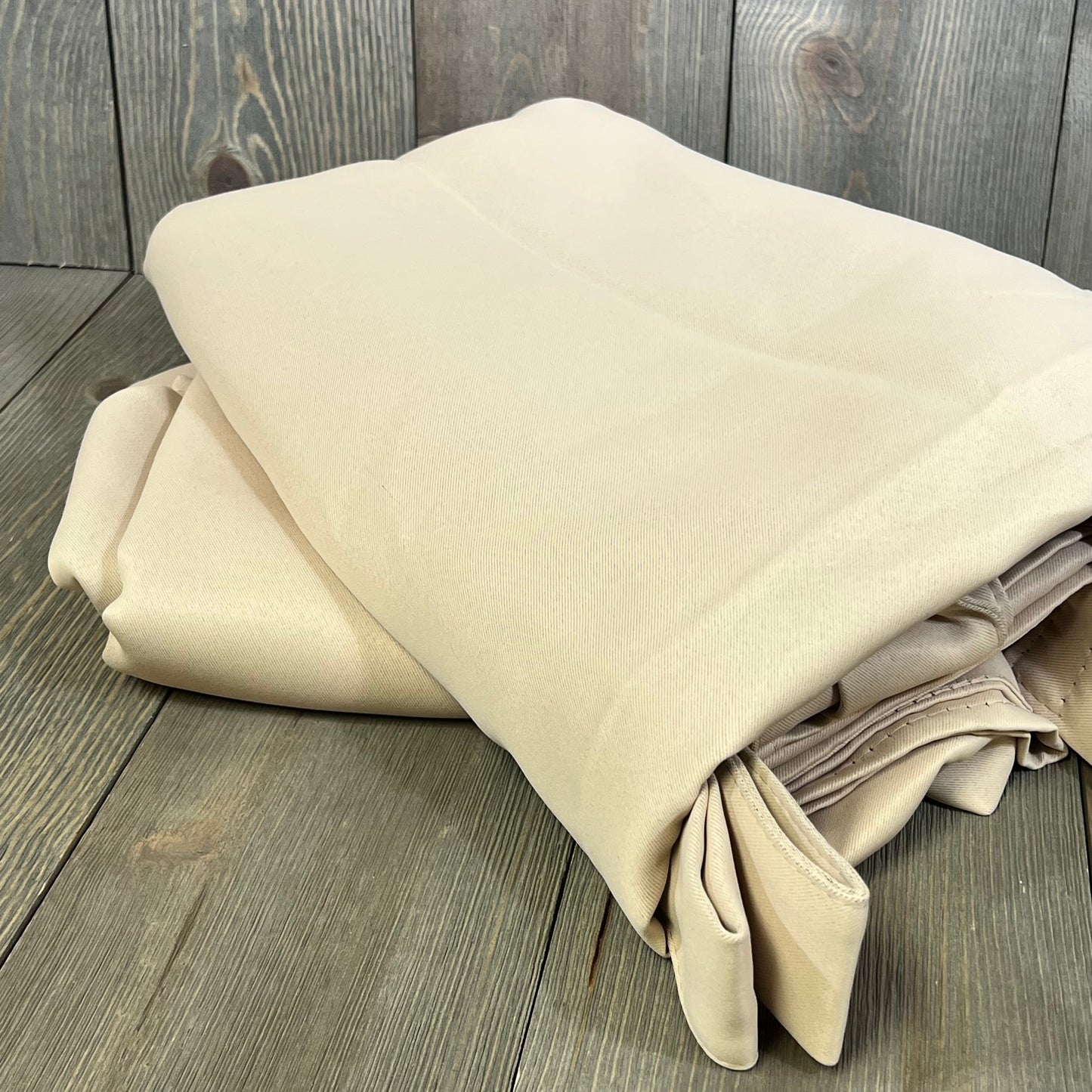 Beige waterproof outdoor curtain panels folded on wooden surface, ideal for gazebo privacy and patio decor.