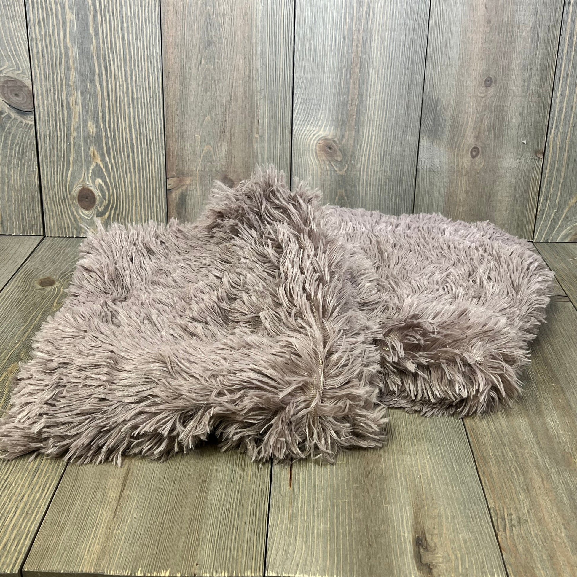 Purplish taupe faux fur pillow covers on rustic wooden surface, featuring soft velvet texture and zipper closure.