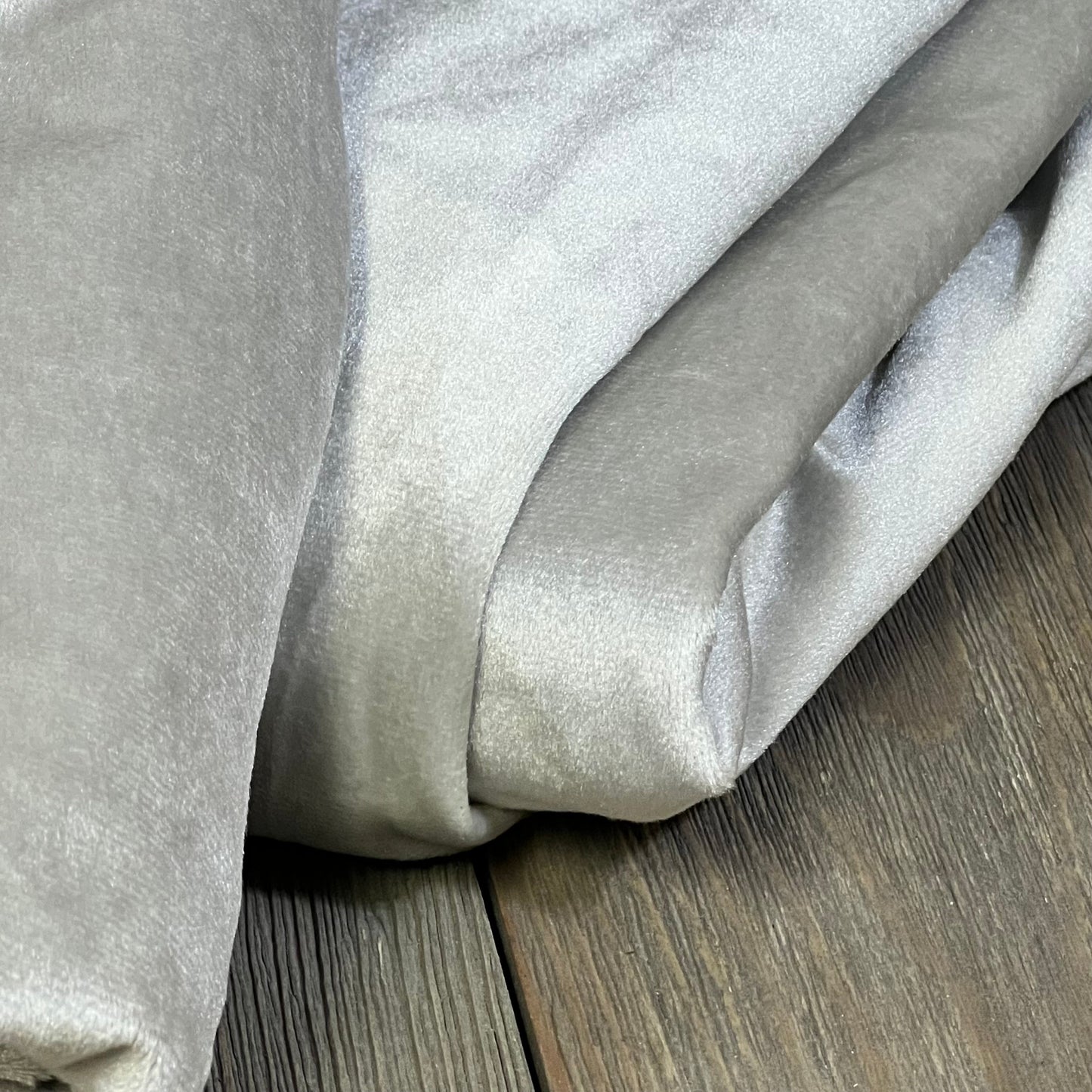 Grey blackout curtains folded on wooden floor, showcasing the soft texture and thermal insulation for living room or bedroom.