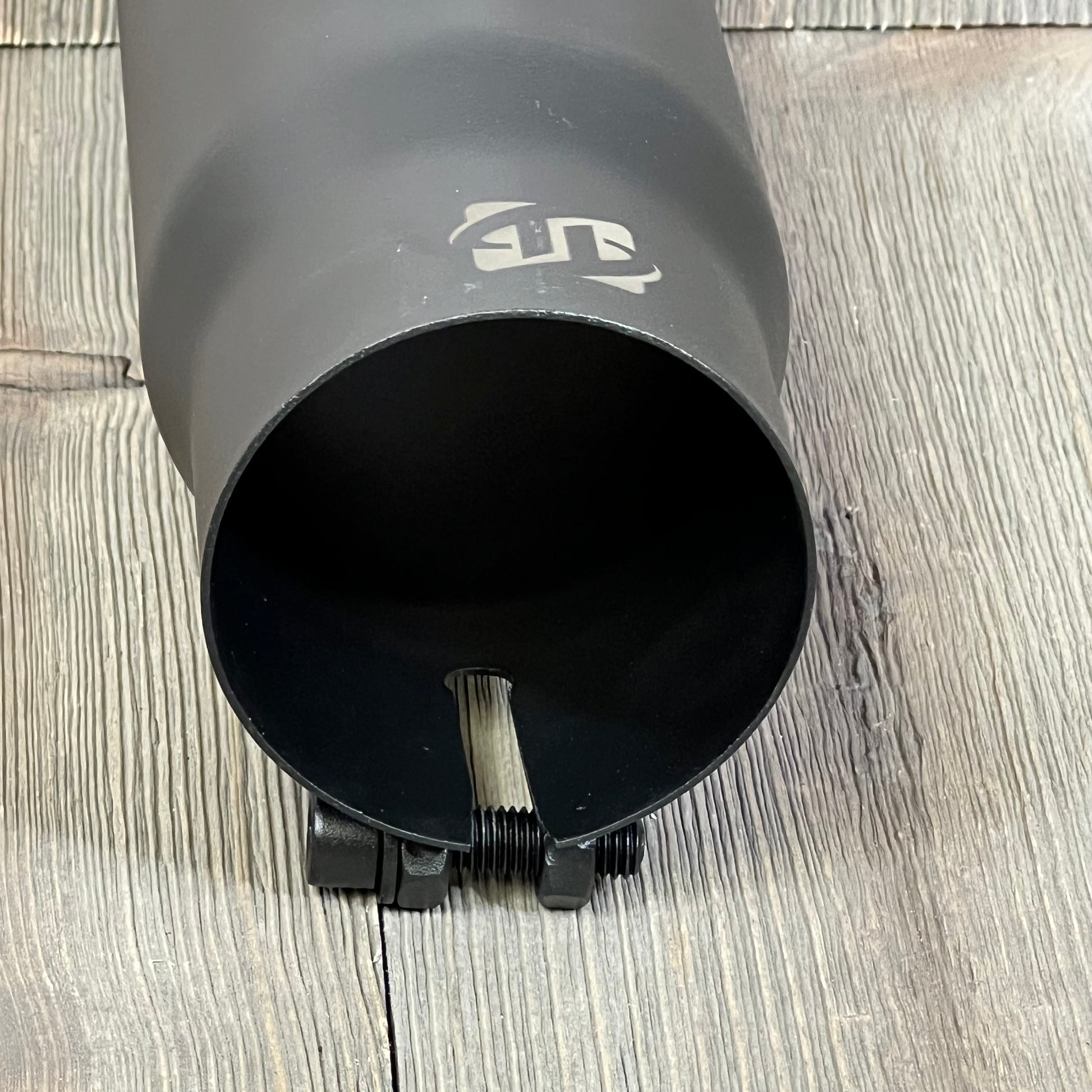 Black exhaust tip with 2.5-inch inlet, bolt-on design, and black coated stainless steel finish on a wooden surface.