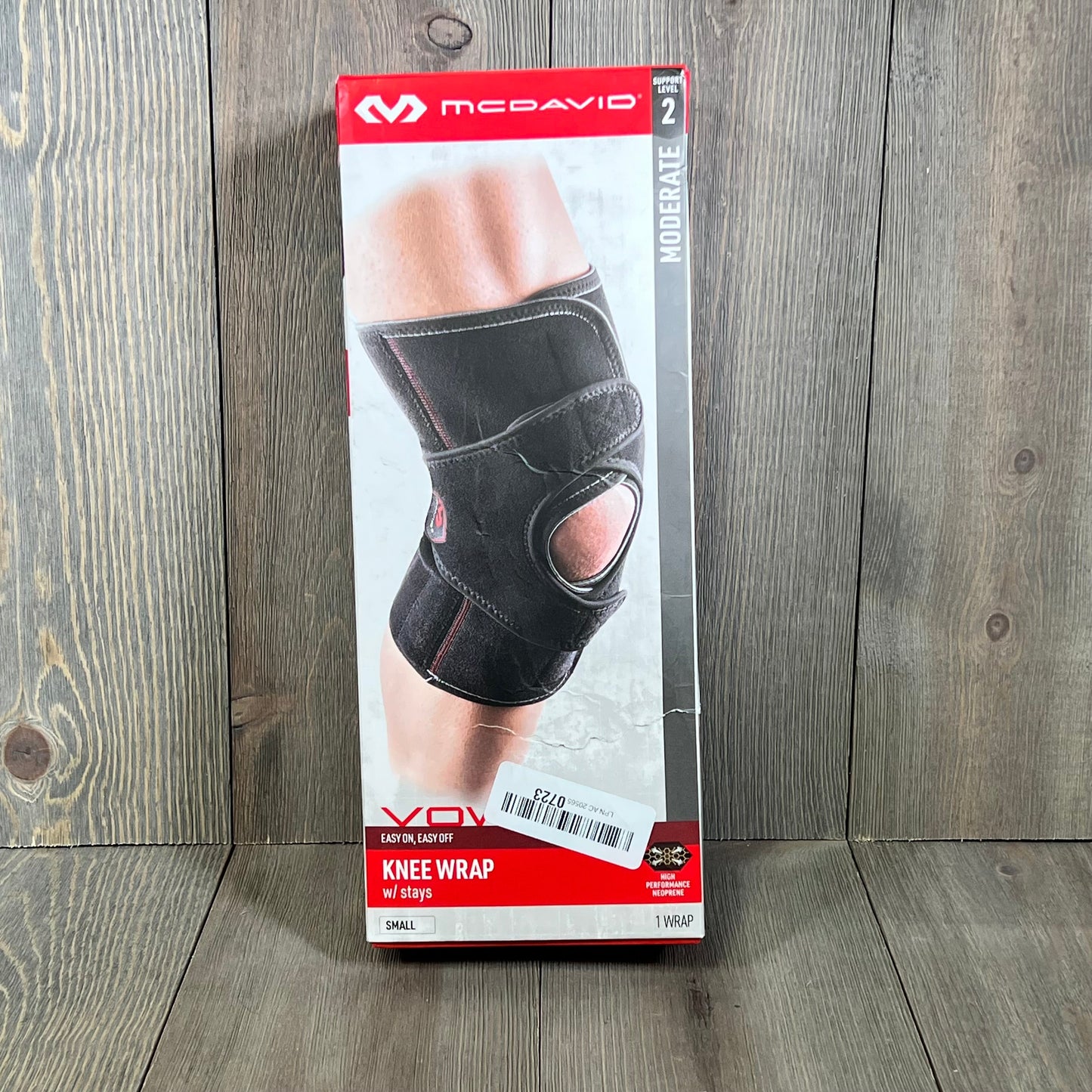 Black McDavid MD4201 knee wrap with stays in small size, shown in packaging against a wooden background.