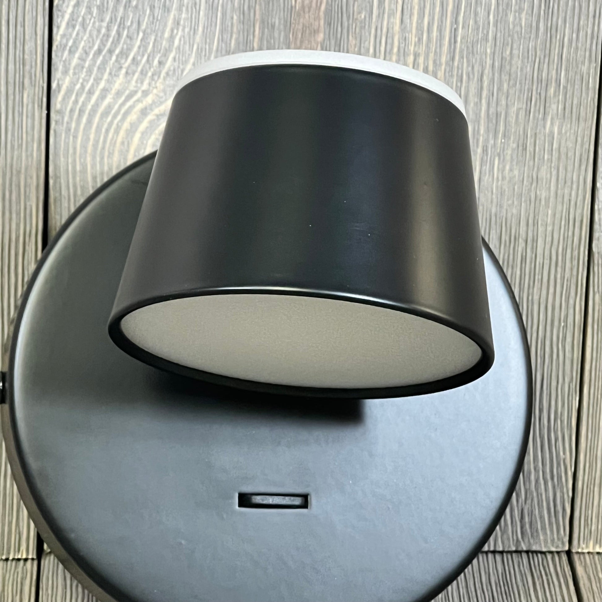 Black URSOLA LED wall sconce with USB port, showcasing a sleek, rotatable design on a wooden background.