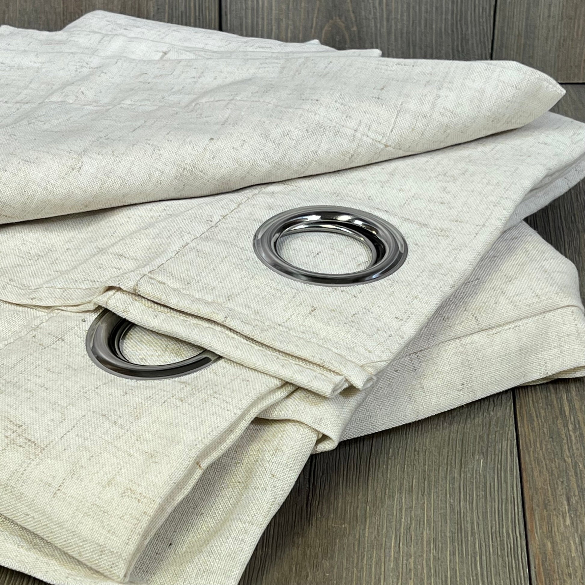 Beige ChrisDowa blackout curtains with silver grommets, perfect for bedrooms and living rooms, folded on wooden floor.