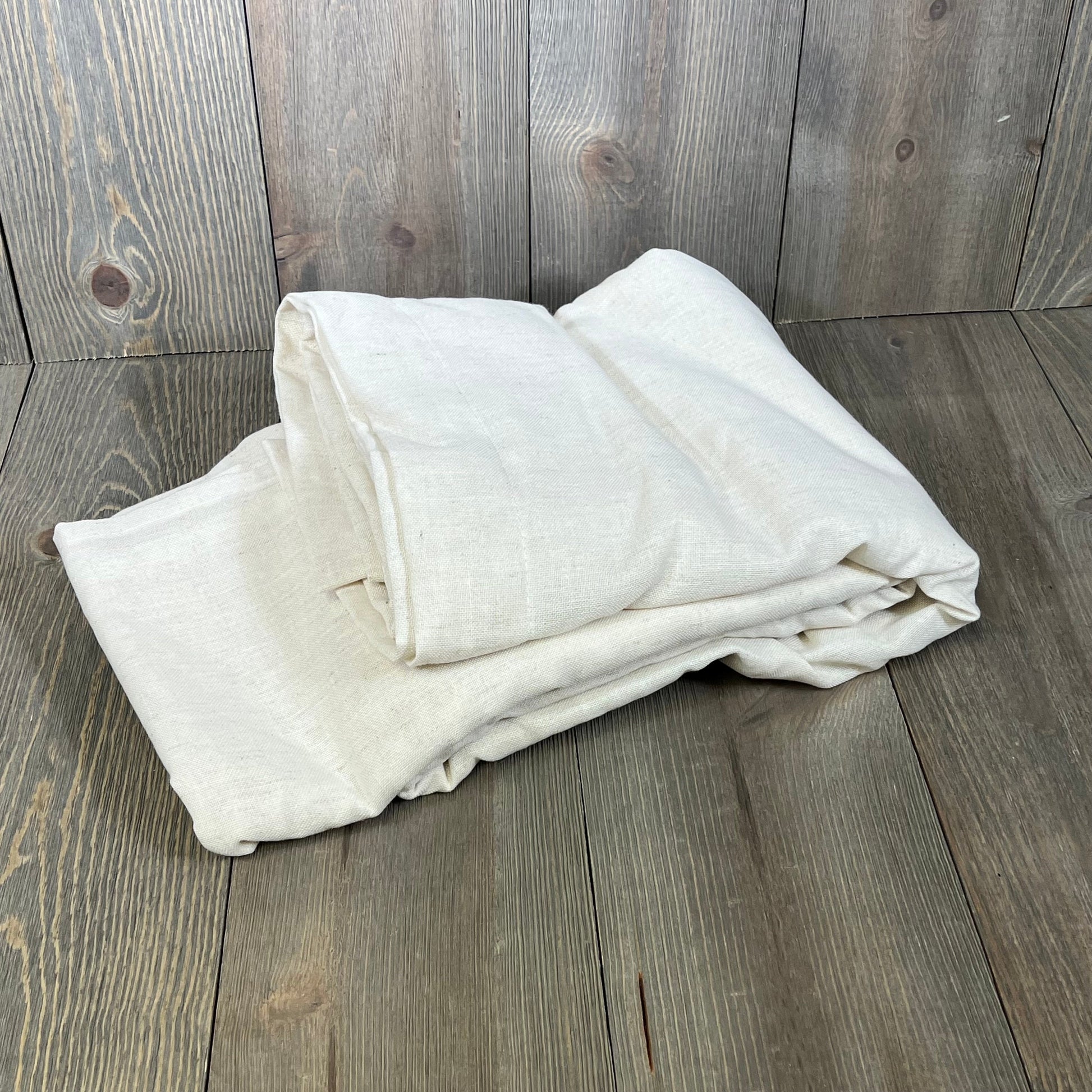 Cream linen drapes folded on wooden floor, showcasing the texture and quality of XTMYI 94-inch sheer curtains set.