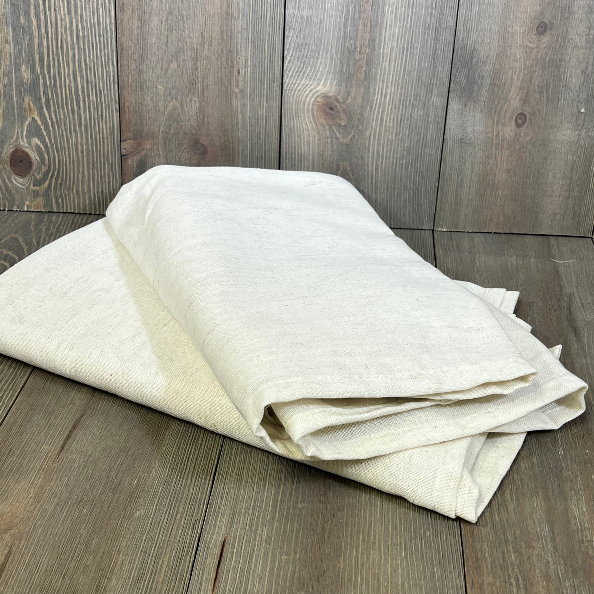 Cream beige linen sheer curtains folded on wooden floor, showcasing light-filtering fabric and semi-transparent design.