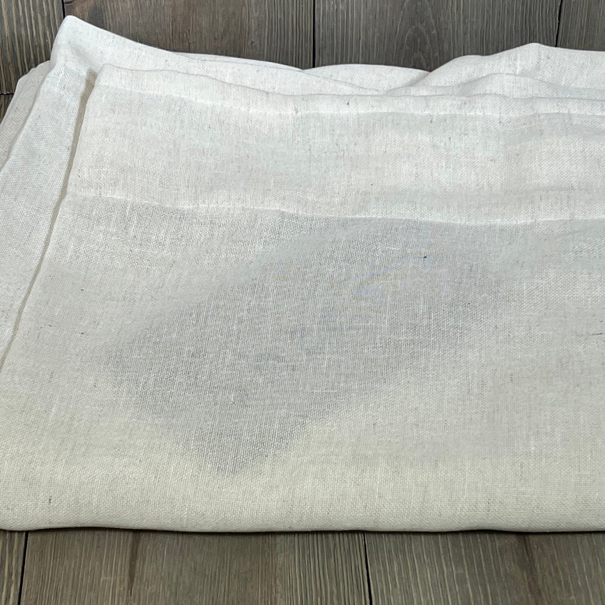 Cream linen drapes folded on a wooden surface, showcasing texture and quality of XTMYI 94-inch sheer curtains.