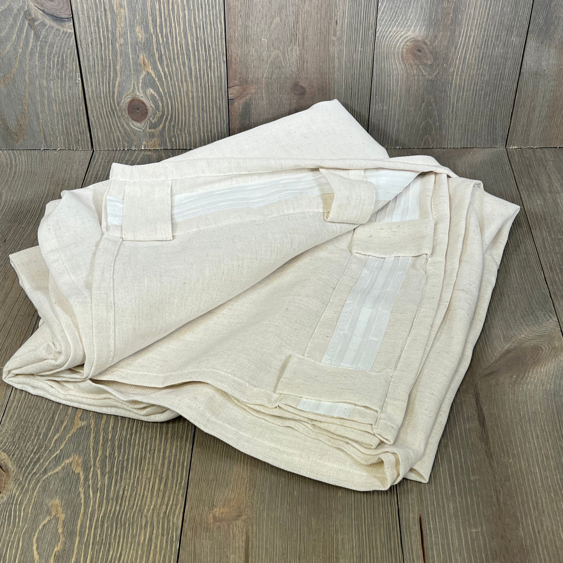 Cream ivory linen drapes folded on wooden floor, showcasing back tab design for easy hanging, 94 inches long.