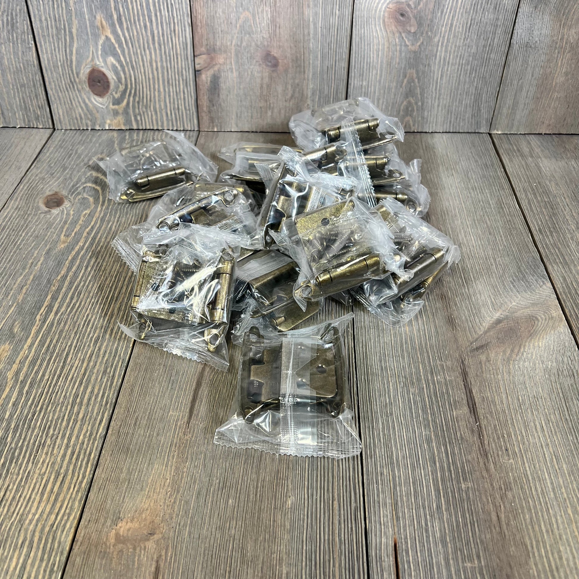 Antique brass cabinet door hinges, 30 pack, shown in packaging on a rustic wooden surface. Perfect for kitchen updates.