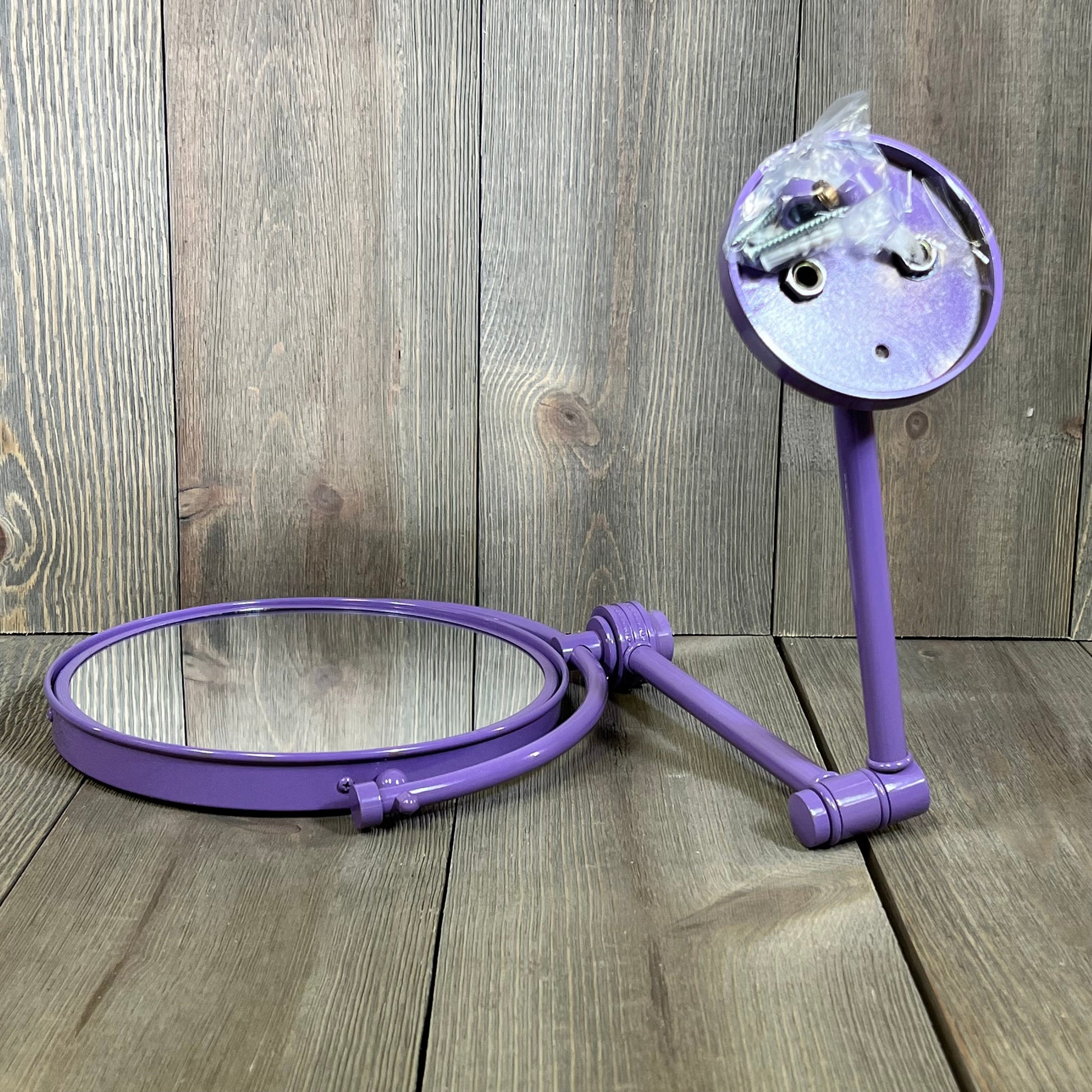 Lavender wall-mounted make-up mirror with 4X magnification and twist accent, displayed on a wooden background.