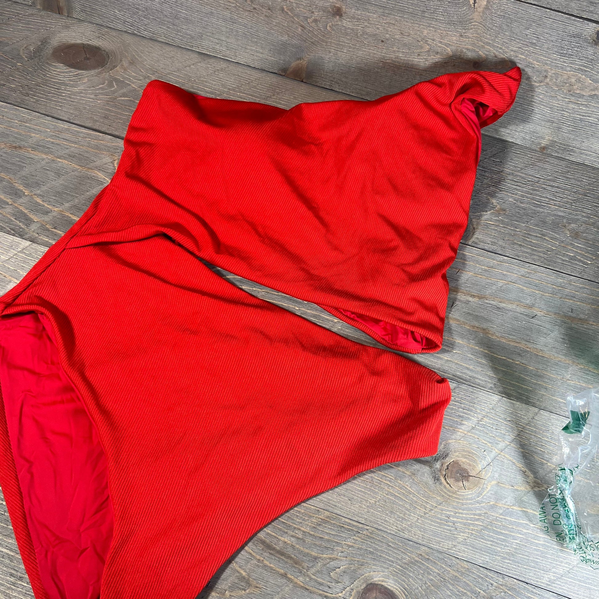 Red one-shoulder ribbed swimsuit with cutout design on wooden background, size XL.