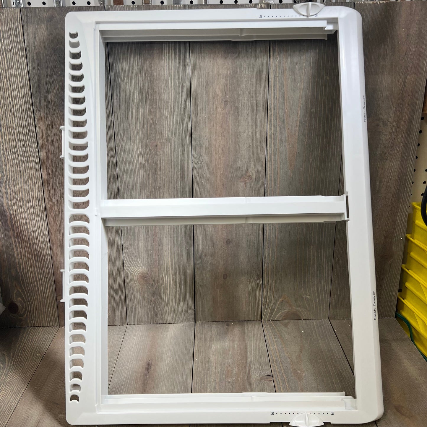 Refrigerator crisper drawer cover frame for Frigidaire, model 1046027509, shown against a wood background.