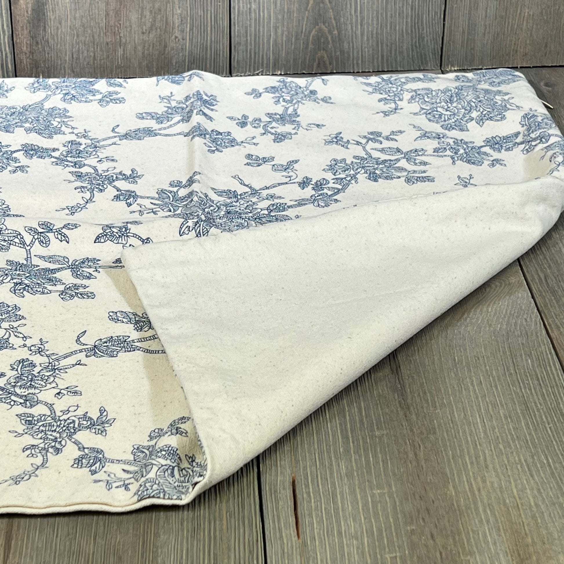Blue floral design on a 100% cotton throw pillow cover, perfect for farmhouse decor, shown on a wooden surface.