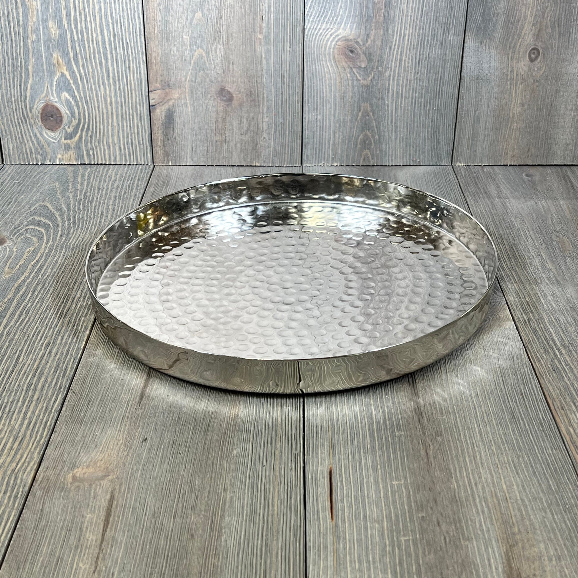 Hammered silver serving tray, 11-inch round, ideal for candles, jewelry, and decor on wooden surface.