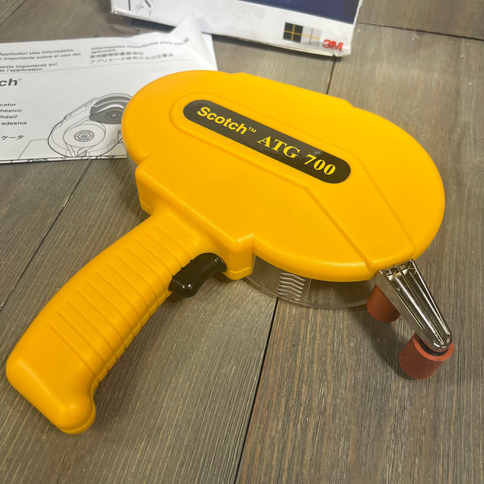 Yellow 3M Scotch ATG 700 Adhesive Applicator on wooden surface, showcasing ergonomic grip and tape roll visibility.