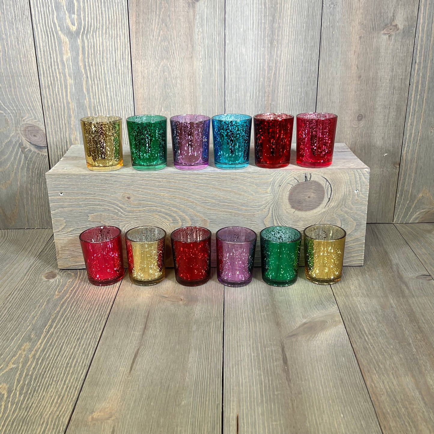 Assorted jewel tone mercury glass votive candle holders, set of 12, displaying deep rich colors on a wooden surface.