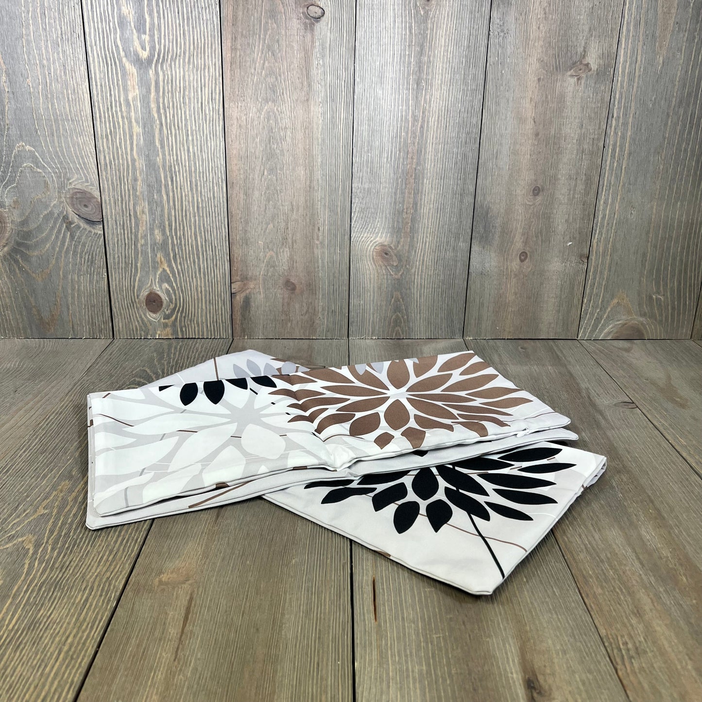 Geometric black and brown outdoor pillow covers on wooden background, ideal for patio furniture and garden decor.