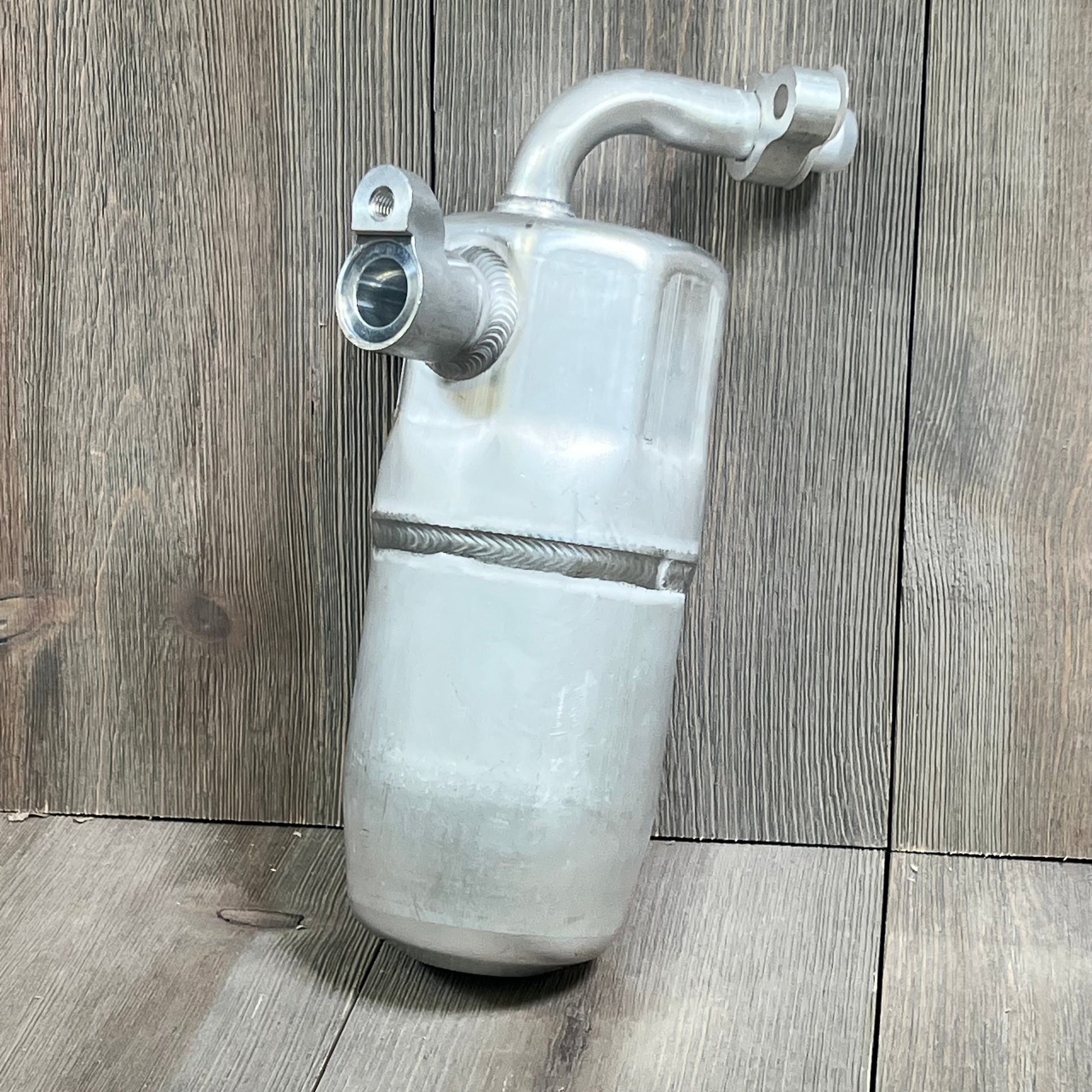 Universal Air Conditioner RD 1801C A/C Accumulator on wooden surface, showcasing its durable metal construction and design.