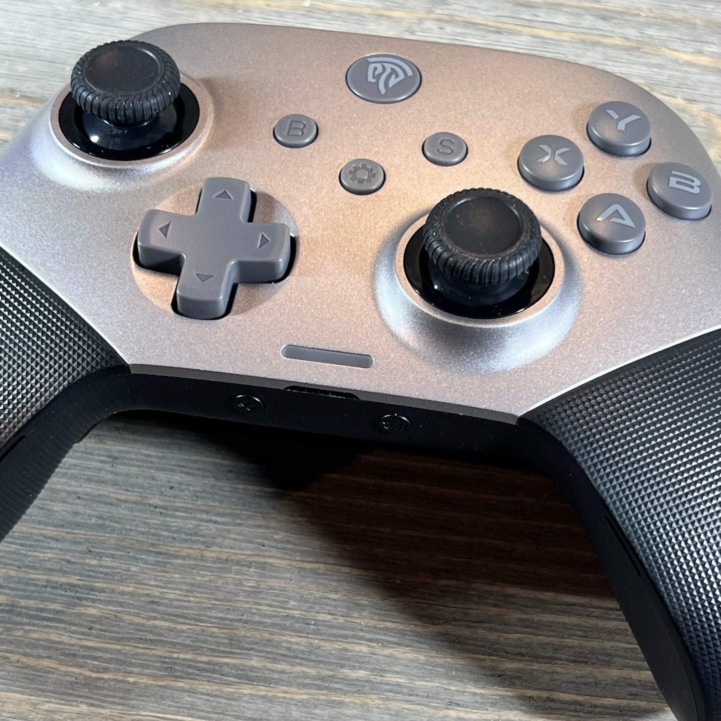 Silver EasySMX X10 wireless Bluetooth controller featuring dual analog sticks and D-pad on a wooden surface.