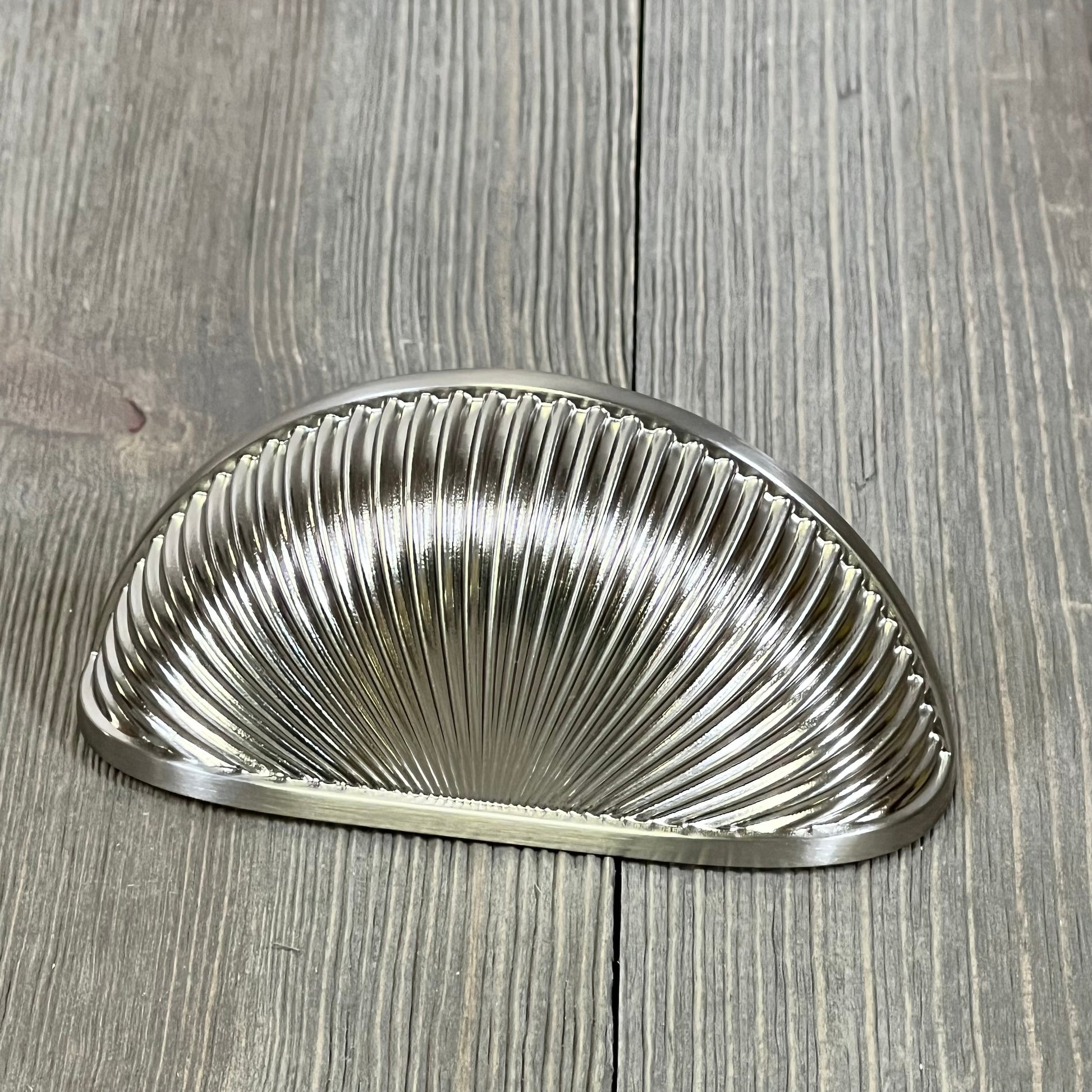 Brushed satin nickel kitchen cabinet handle with a ribbed design on a rustic wooden surface.