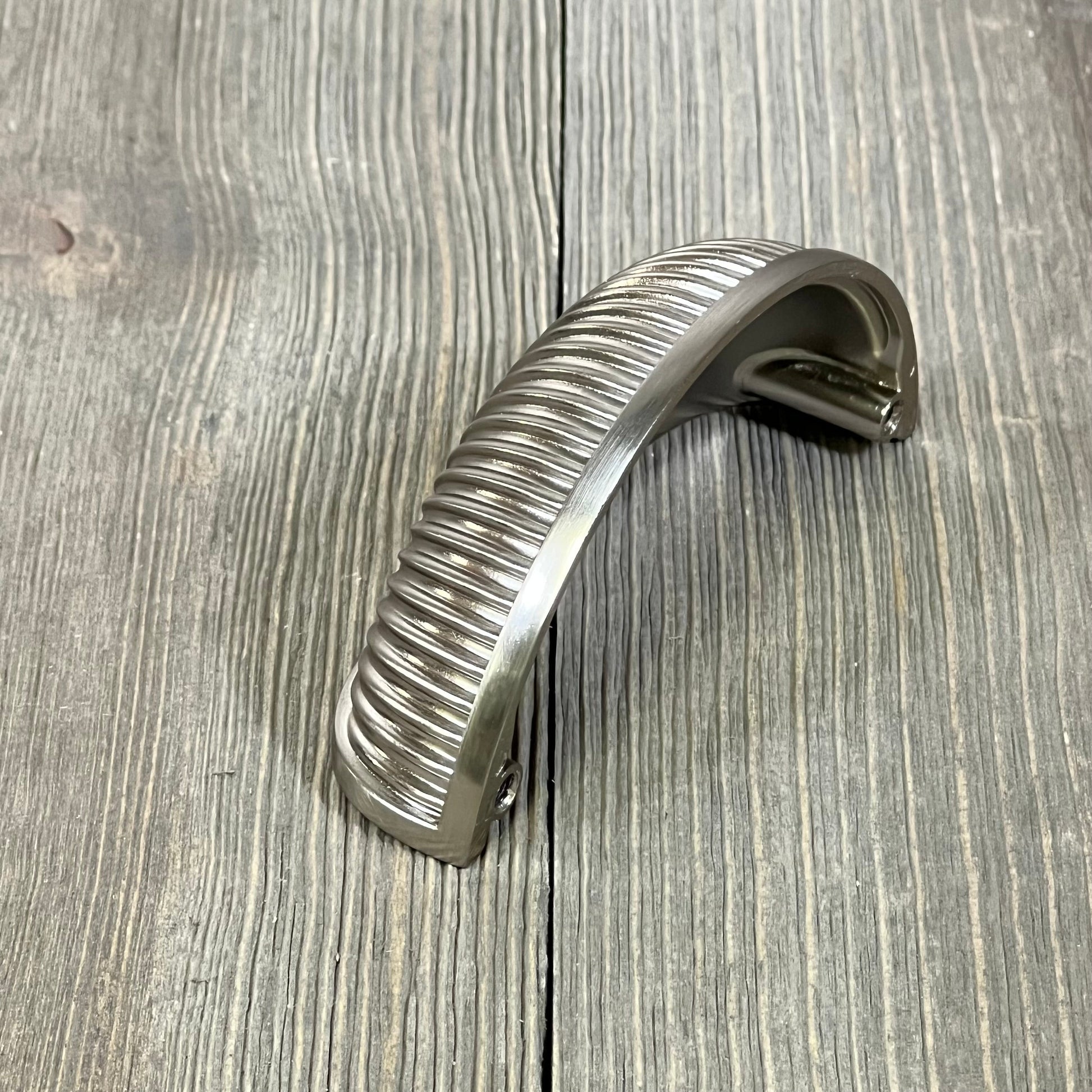 Brushed satin nickel kitchen cabinet handle with ribbed design on rustic wood surface.