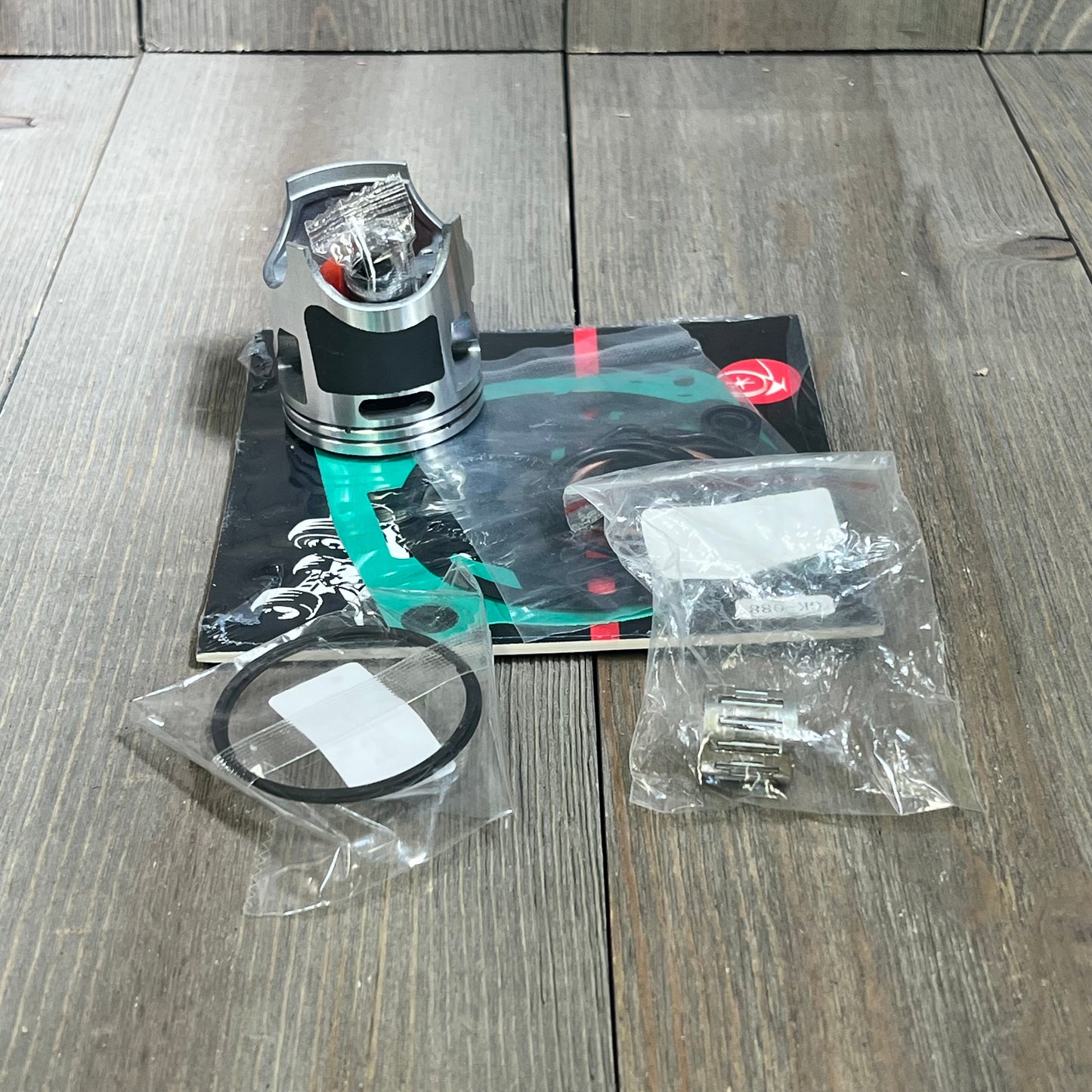 Piston and gasket kit for Kawasaki KX85 2001-2013, includes rings and bearings, displayed on wooden surface.