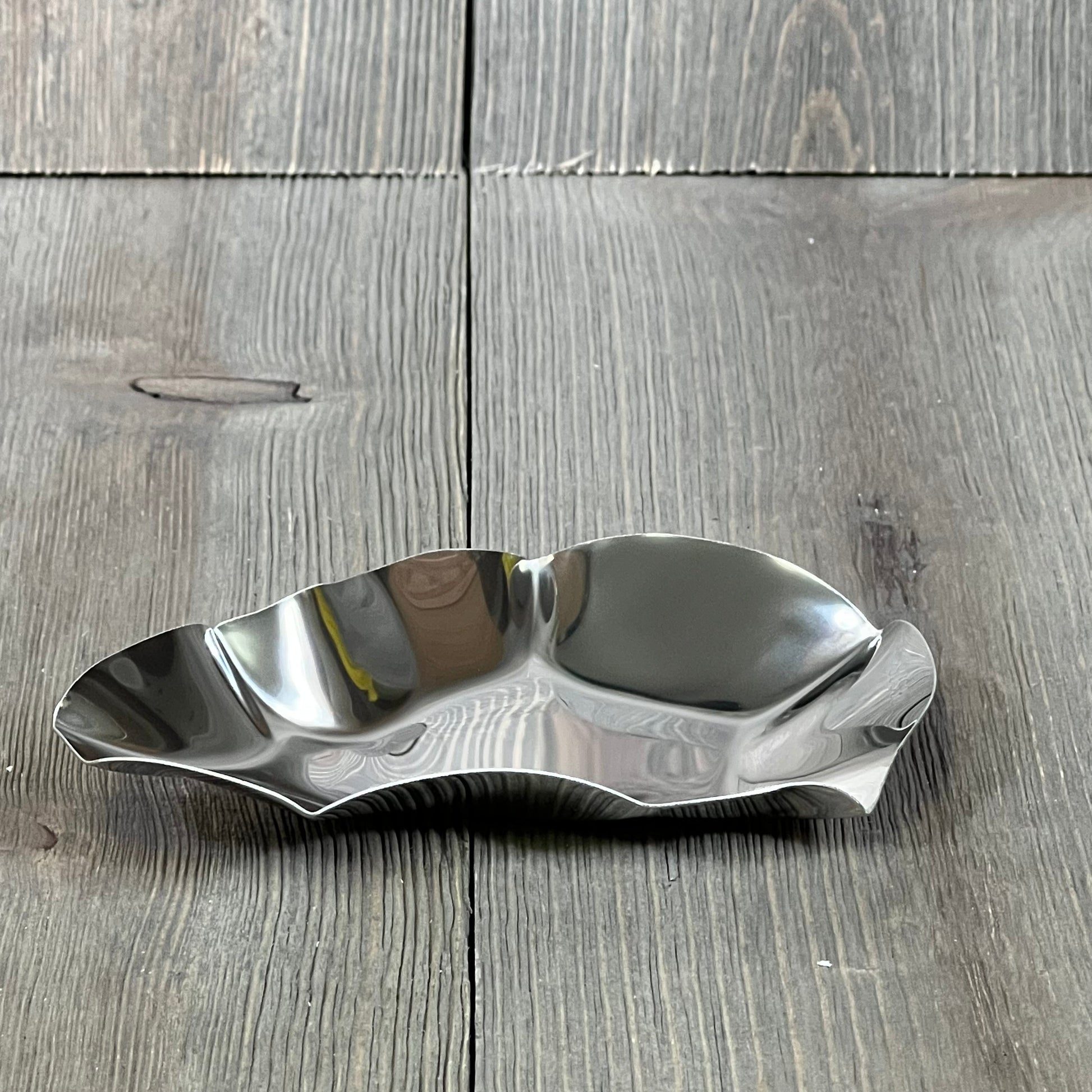 Stainless steel oyster grilling shell on a rustic wooden surface, ideal for cooking and baking seafood dishes.