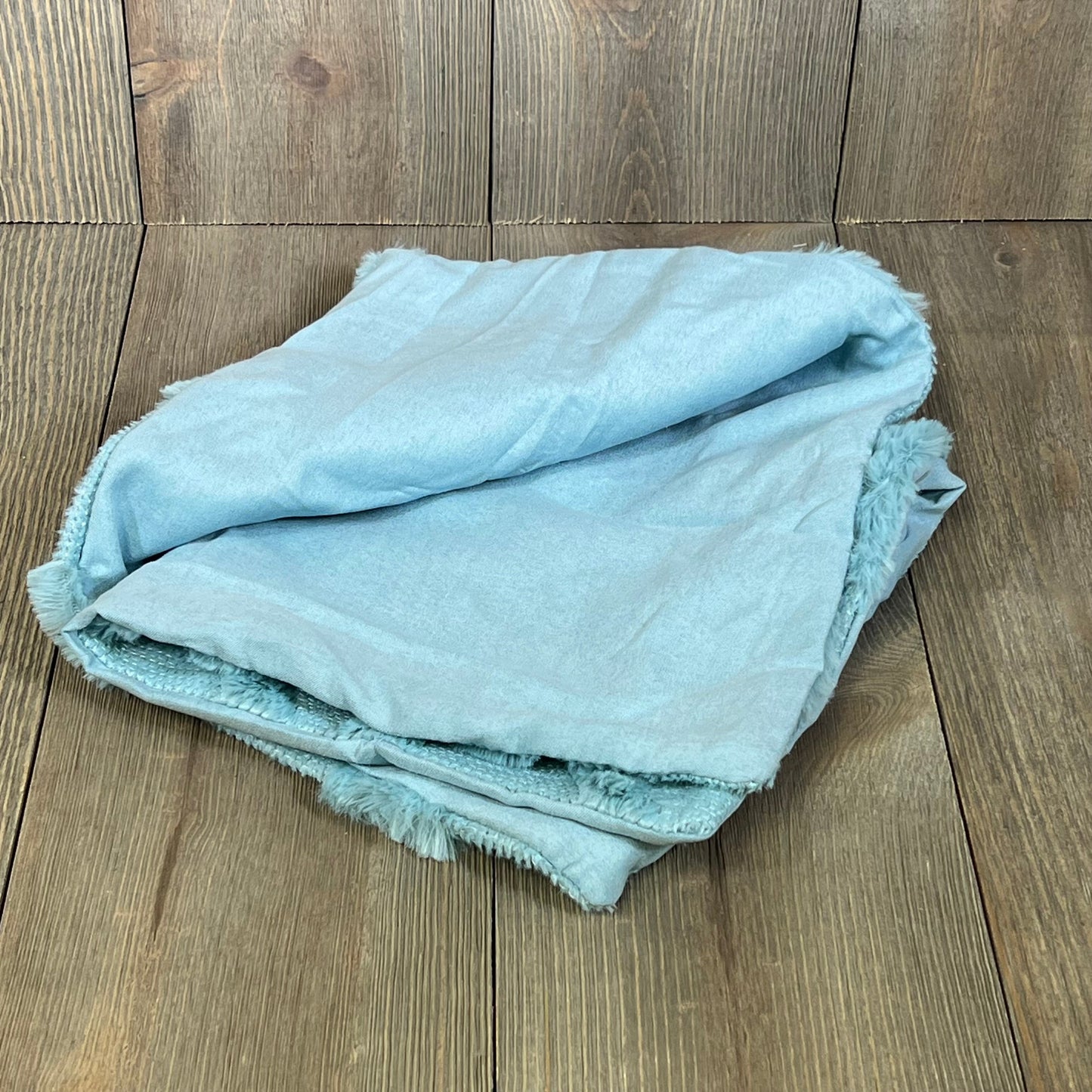 Sky blue faux wool throw pillow covers folded on wooden background, adding a soft, plush touch to farmhouse decor.