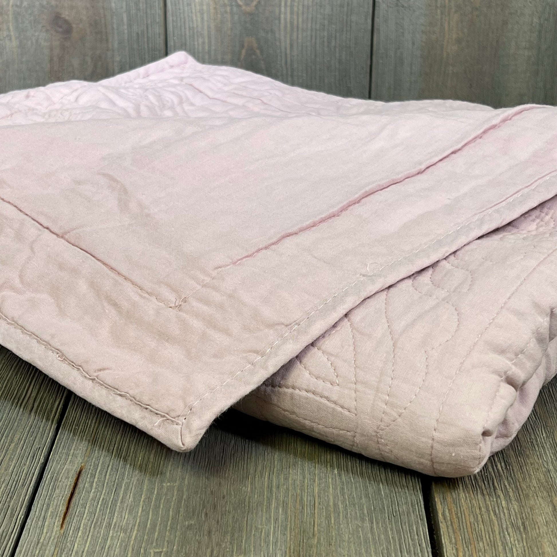 Dusty pink quilted pillow sham in soft cotton, showcasing floral print design on rustic wooden background.