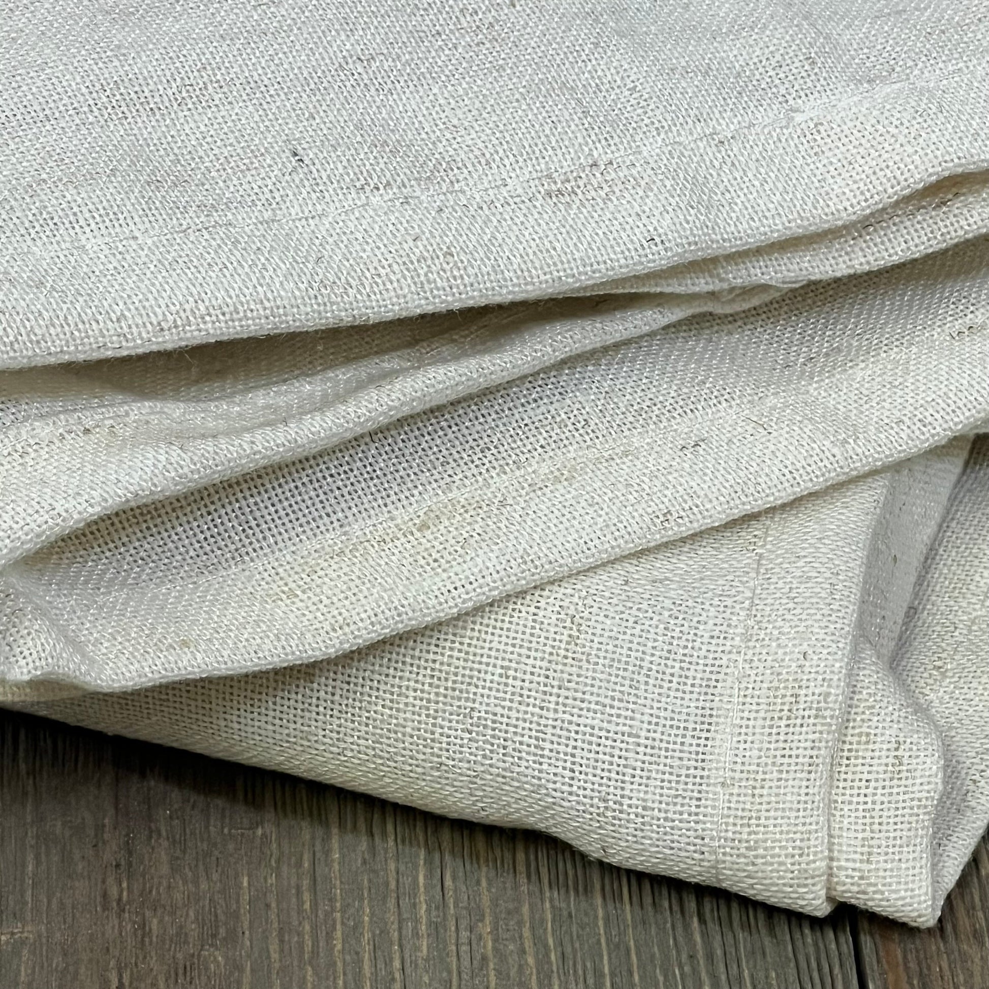 Cream beige linen sheer curtains folded, showcasing texture and semi-transparent quality, ideal for bedroom or living room decor.
