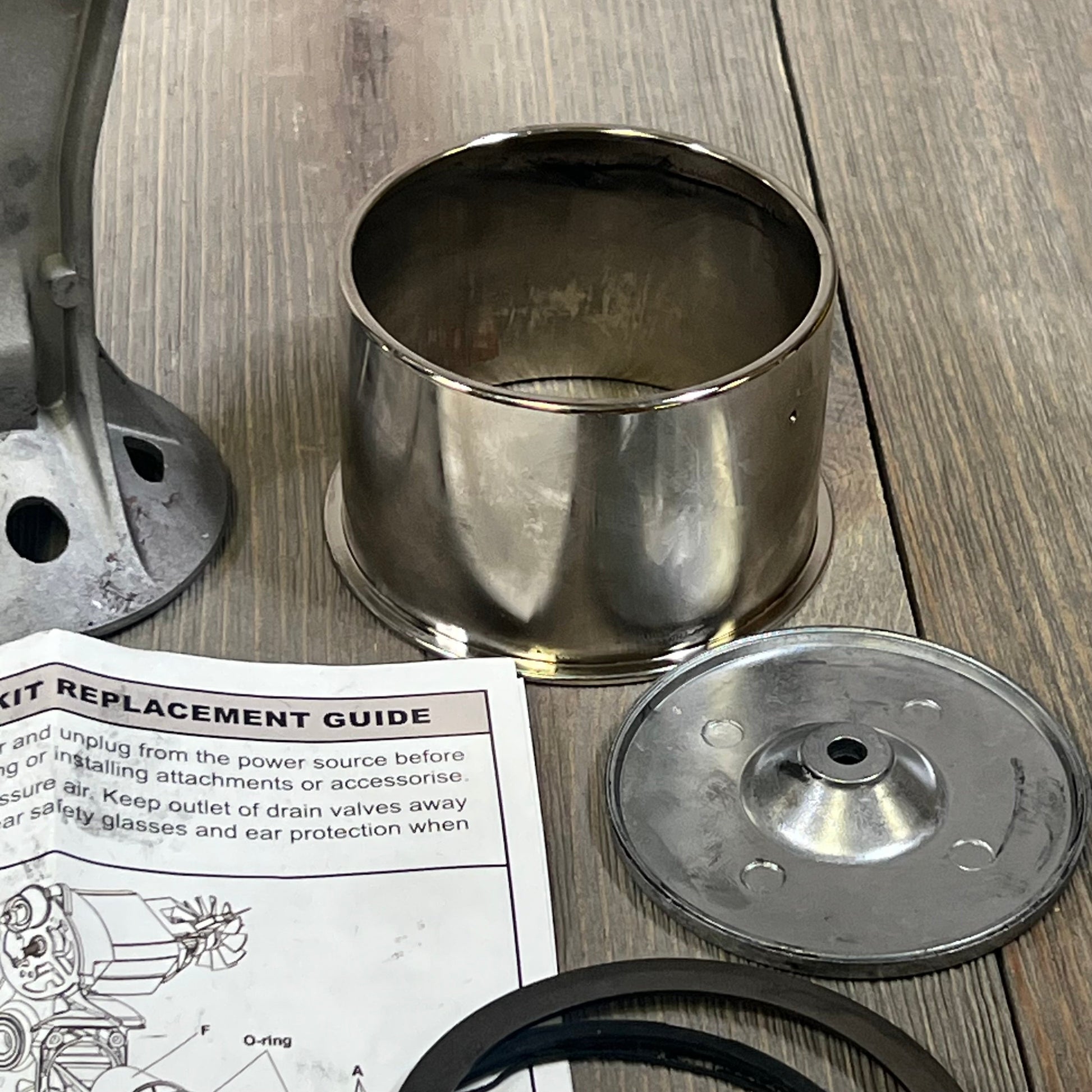 Air compressor piston rod parts with 73 mm cylinder and replacement guide on wooden surface, ideal for repair kits.