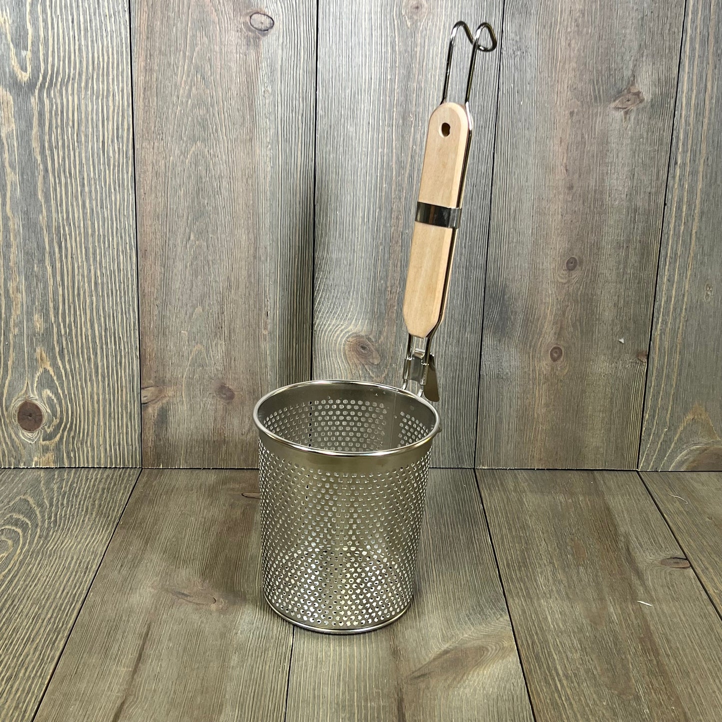 Stainless steel pasta cooker basket with a wood handle, ideal for straining noodles and dumplings, on a wooden surface.