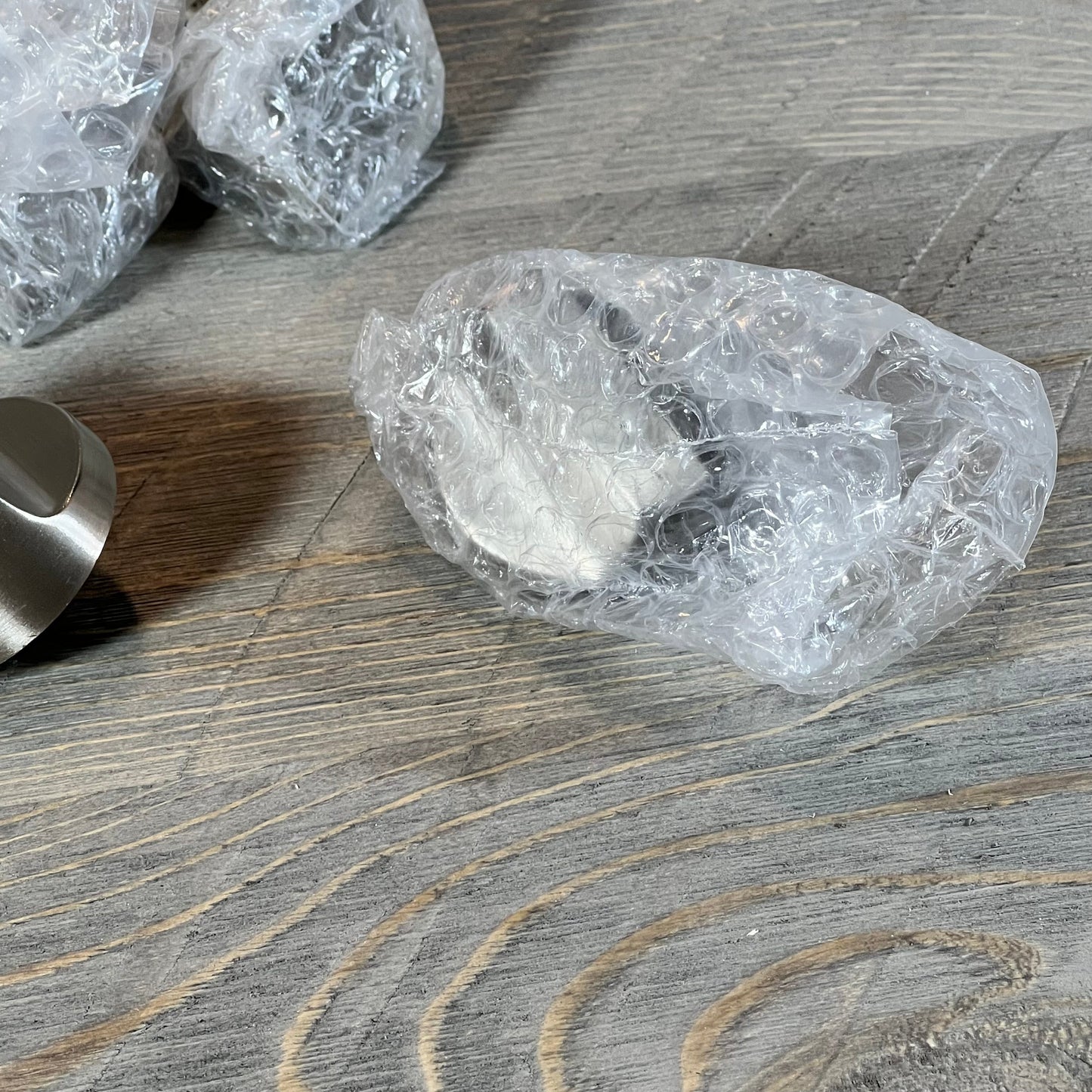 Stainless steel stove knobs for Whirlpool gas range in protective bubble wrap on wooden surface.