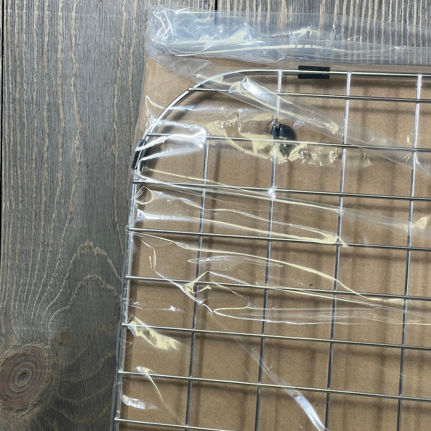 Stainless steel sink protector grid wrapped in plastic, featuring durable construction for kitchen sink protection.